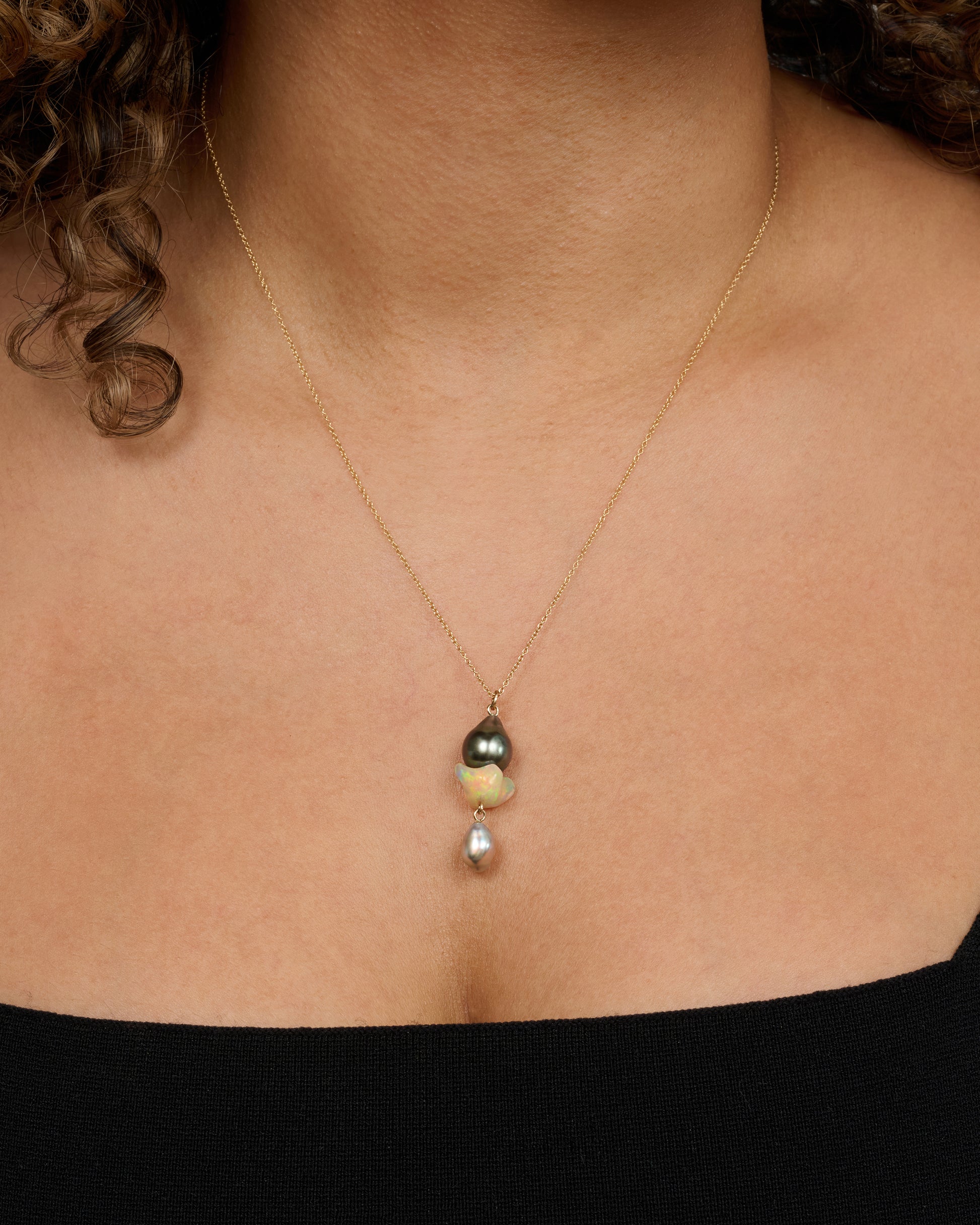 A yellow gold necklace with a triple drop pendant consisting of one opal and two pearls. View on a neck.