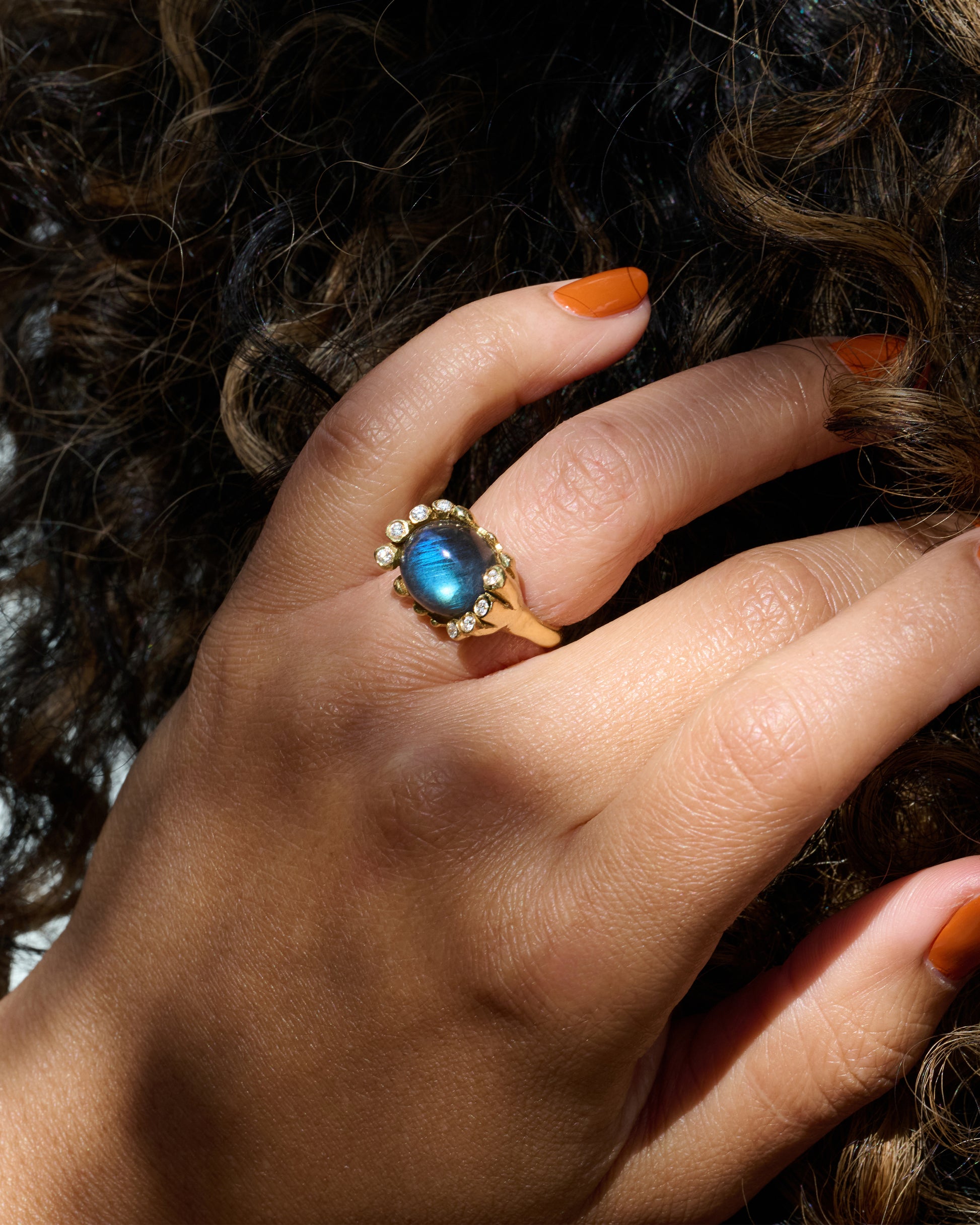 An iridescent labradorite cabochon is nestled amongst diamonds in its handcrafted setting. Shown on hand.