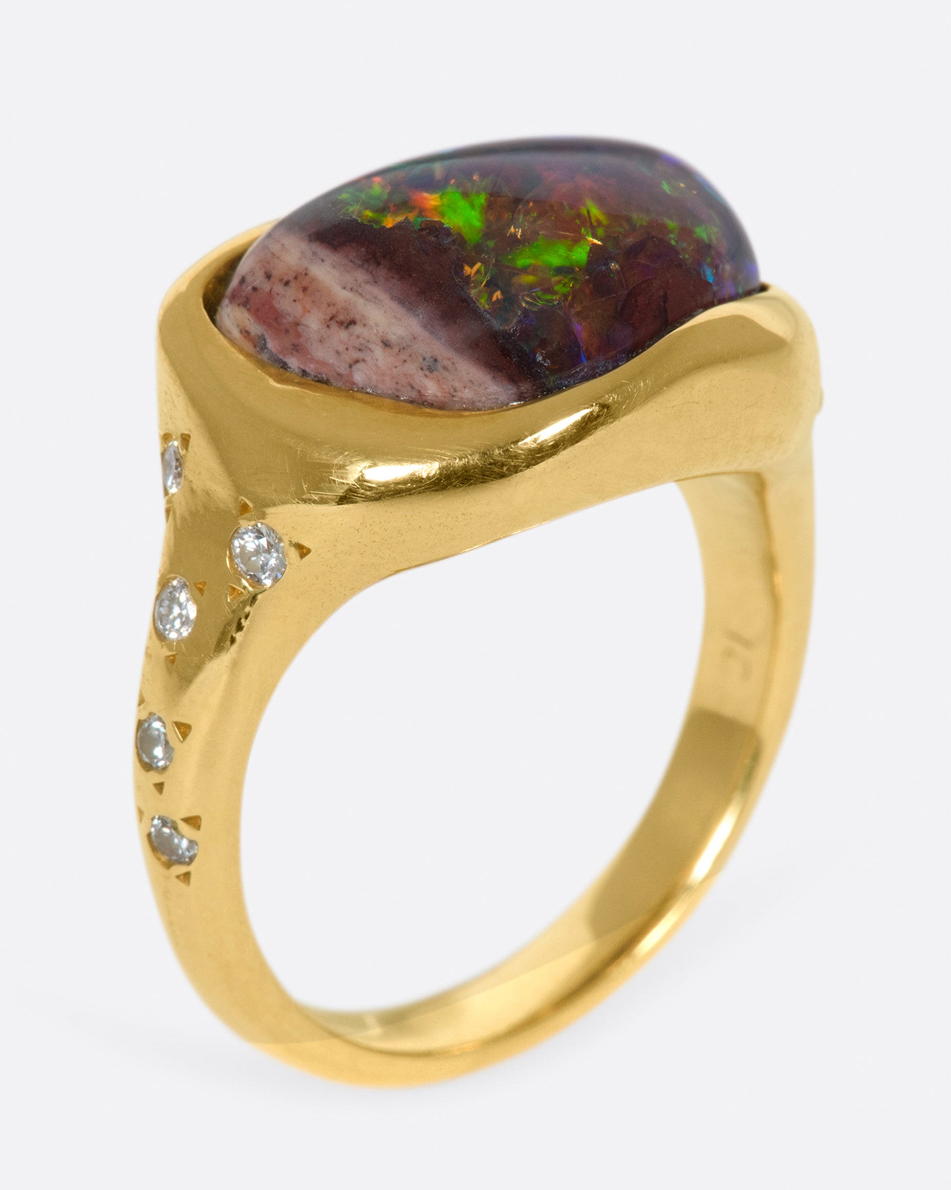 A gold ring with a bezel set curved black opal and round diamond accents.