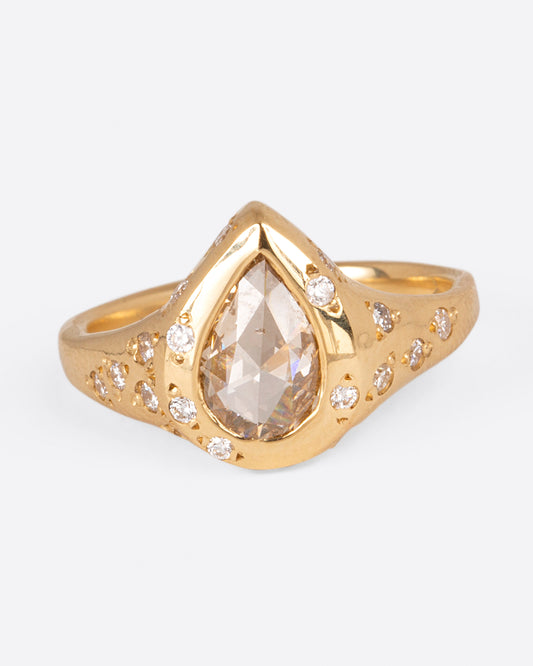A yellow gold ring with a pear shaped diamond center stone and round white diamonds dotting the band, shown from the front.