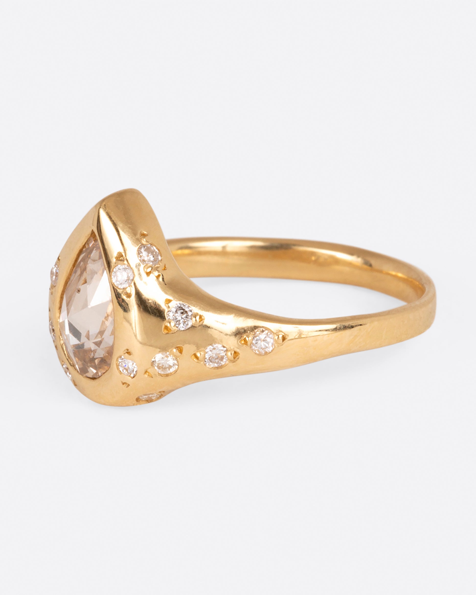 A yellow gold ring with a pear shaped diamond center stone and round white diamonds dotting the band, shown from the side.
