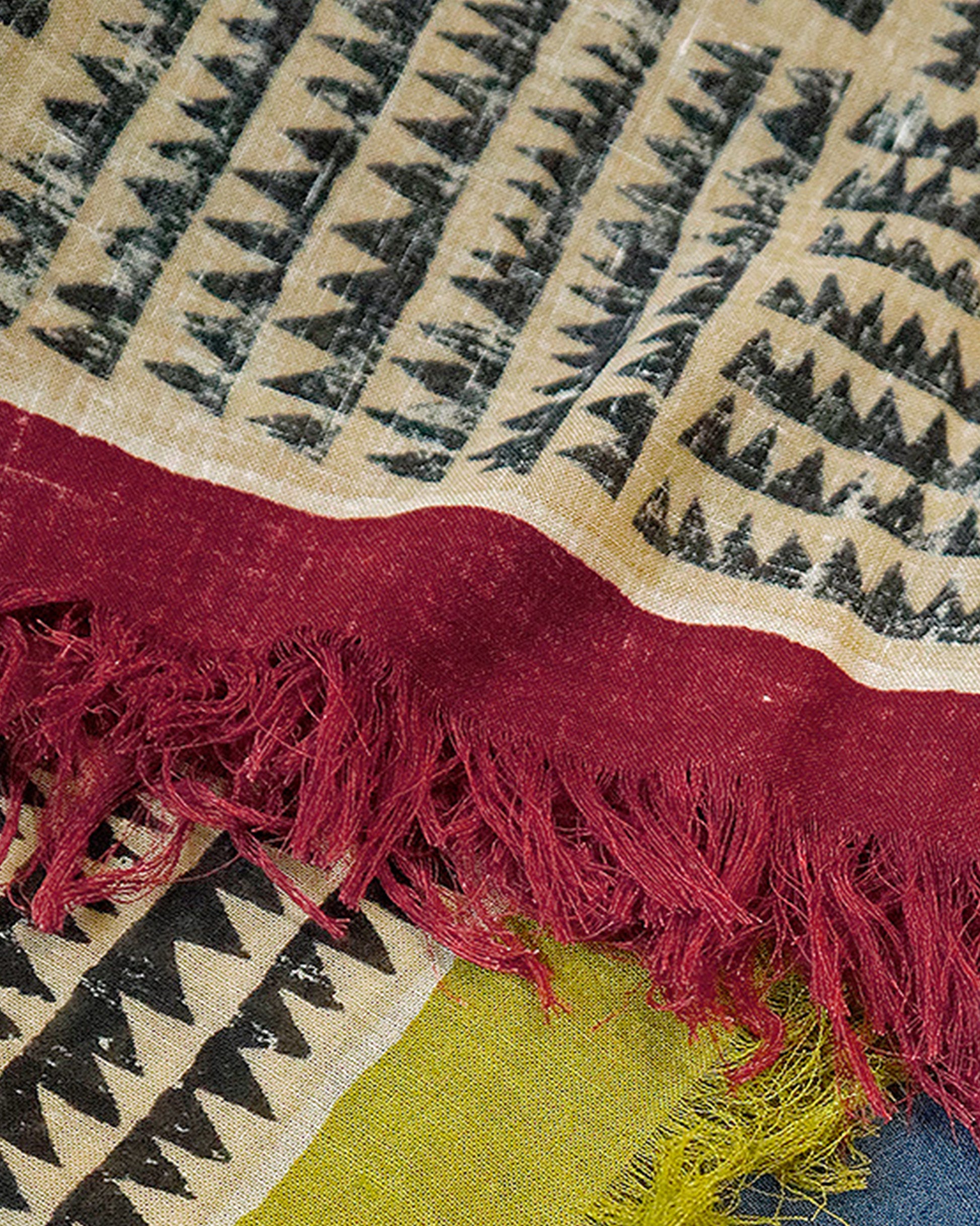 A large, fringy stole covered in a sawtooth block pattern with cranberry red edges.​