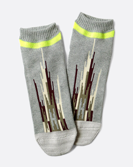A pair of light gray socks that hit mid-ankle with an Ortega pattern across the top of the foot in shades of brown, and a neon green band at the top.