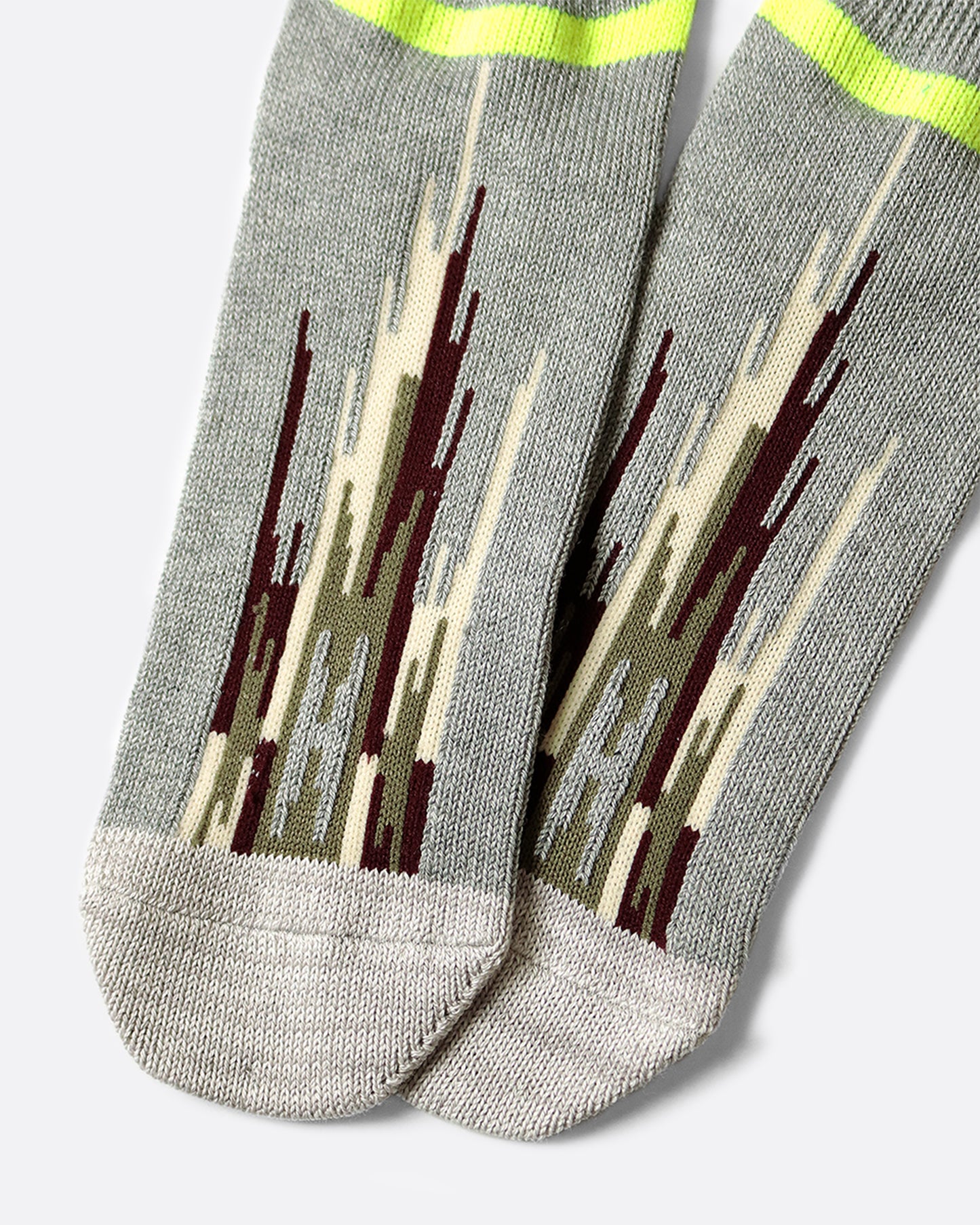 A pair of light gray socks that hit mid-ankle with an Ortega pattern across the top of the foot in shades of brown, and a neon green band at the top.