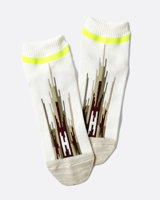 A pair of white socks that hit mid-ankle with an Ortega pattern across the top of the foot in shades of brown, and a neon green band at the top.