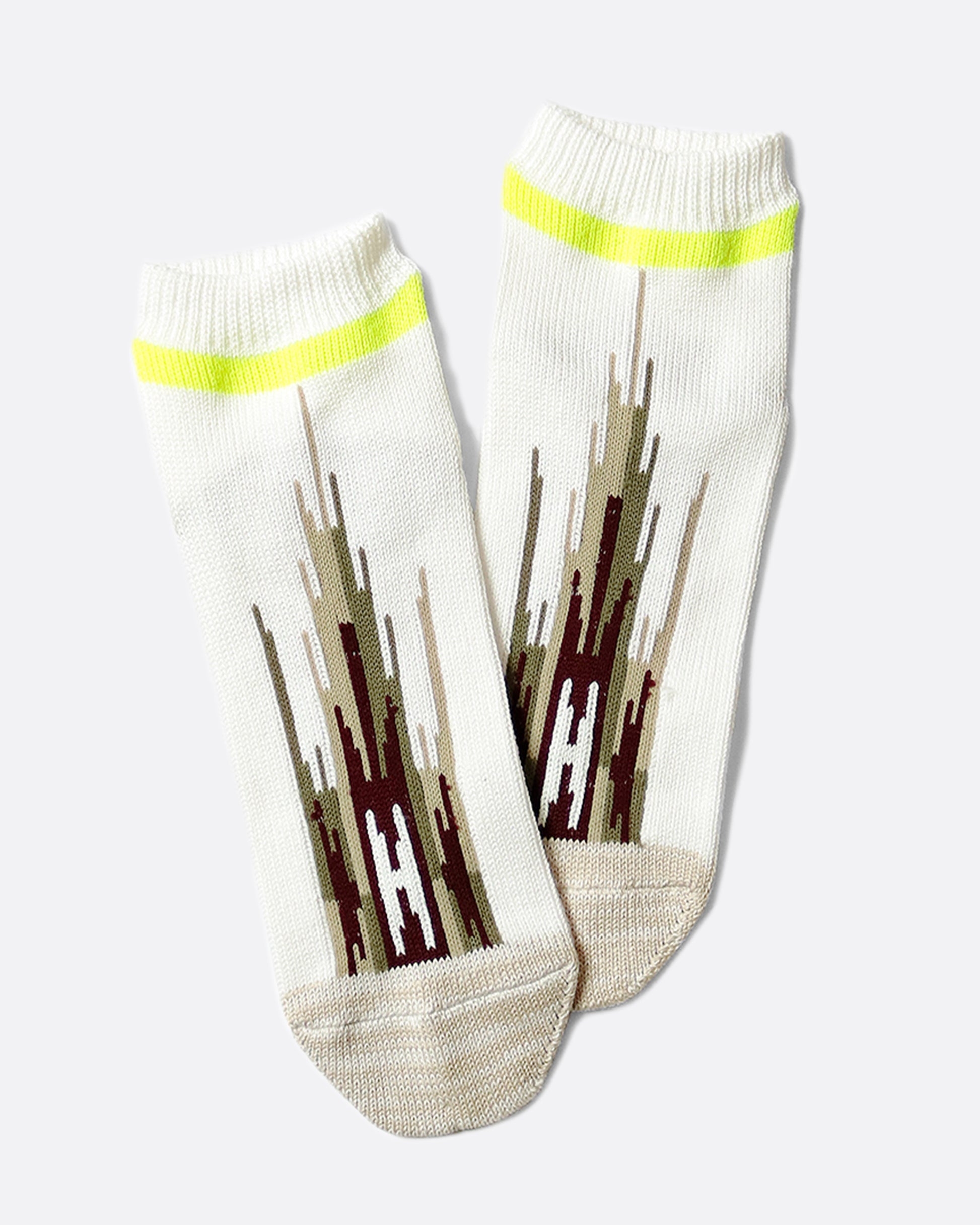 A pair of white socks that hit mid-ankle with an Ortega pattern across the top of the foot in shades of brown, and a neon green band at the top.