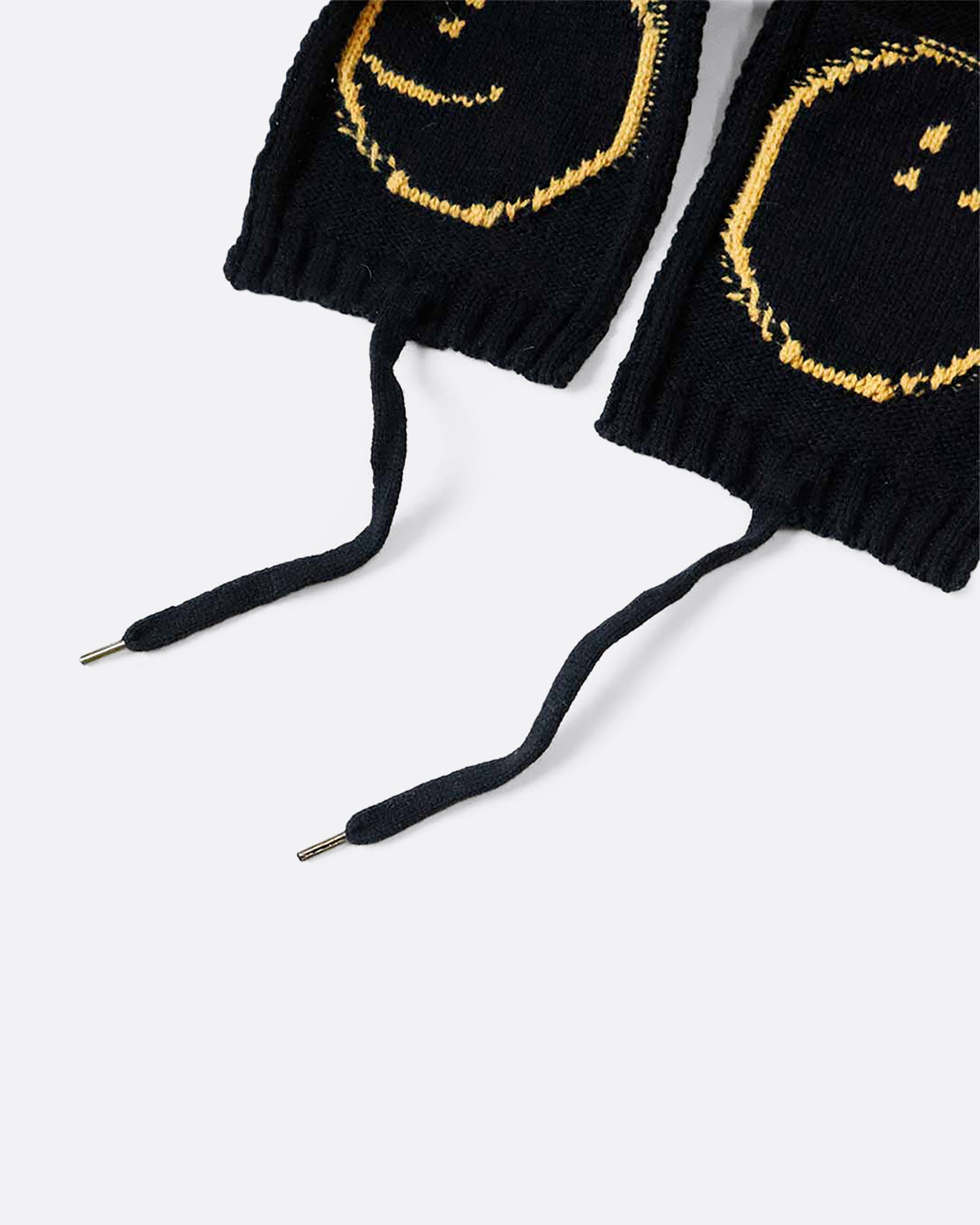 A black knit hat with yellow smilie faces on either ear flap. View close up of the ties.