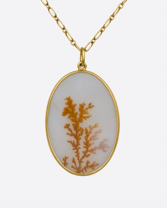 A yellow gold necklace with oval dendritic agate pendant on a yellow gold chain. View up close from the front.