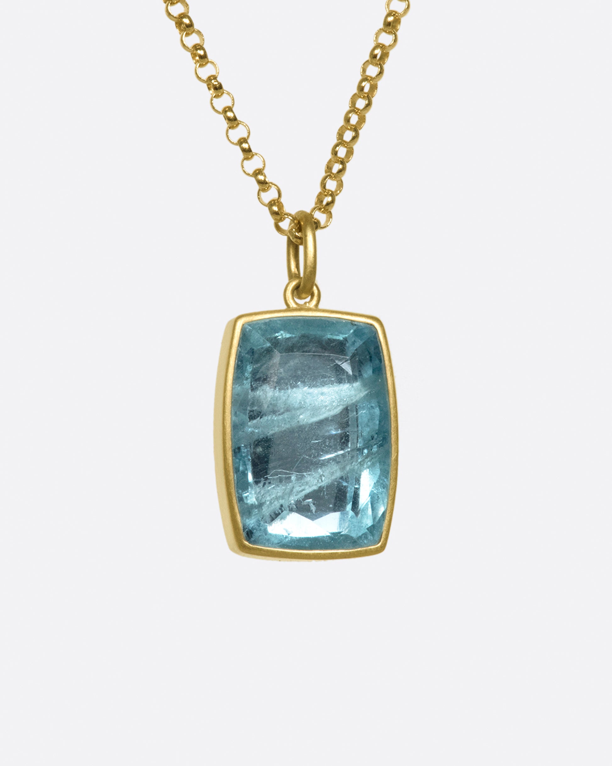 A close up side view of a cushion shaped aquamarine pendant with a yellow gold bezel on a gold chain.