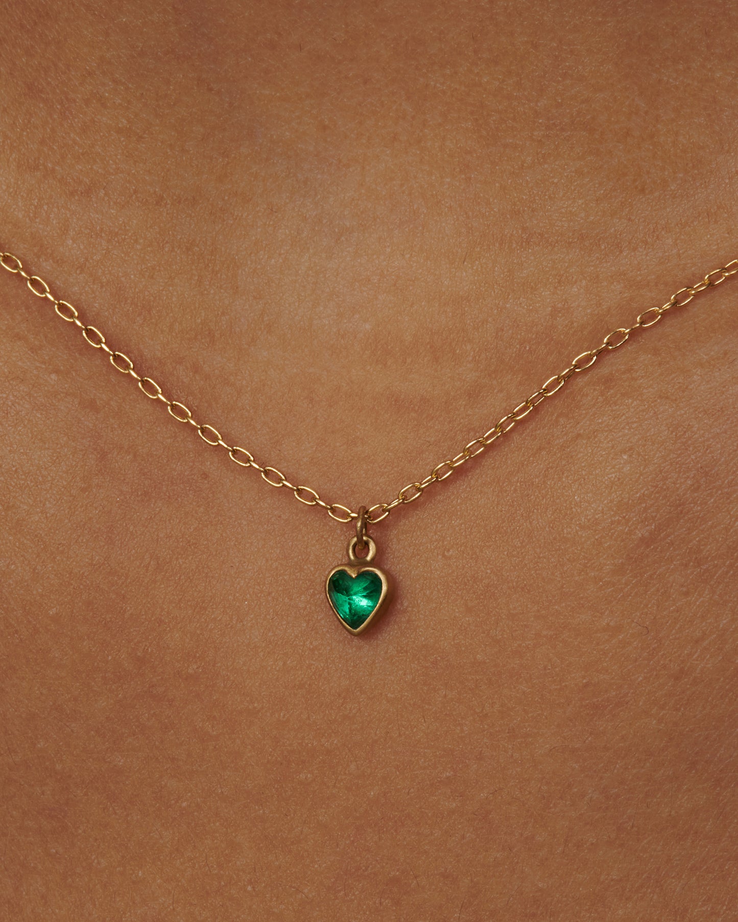 A dainty Colombian emerald heart pendant sweetly swinging on a brushed gold chain.