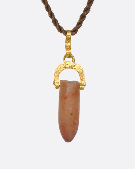 A stunning pre-Columbian carnelian bullet pendant suspended in 22k gold from a lengthy, twisted brown chord