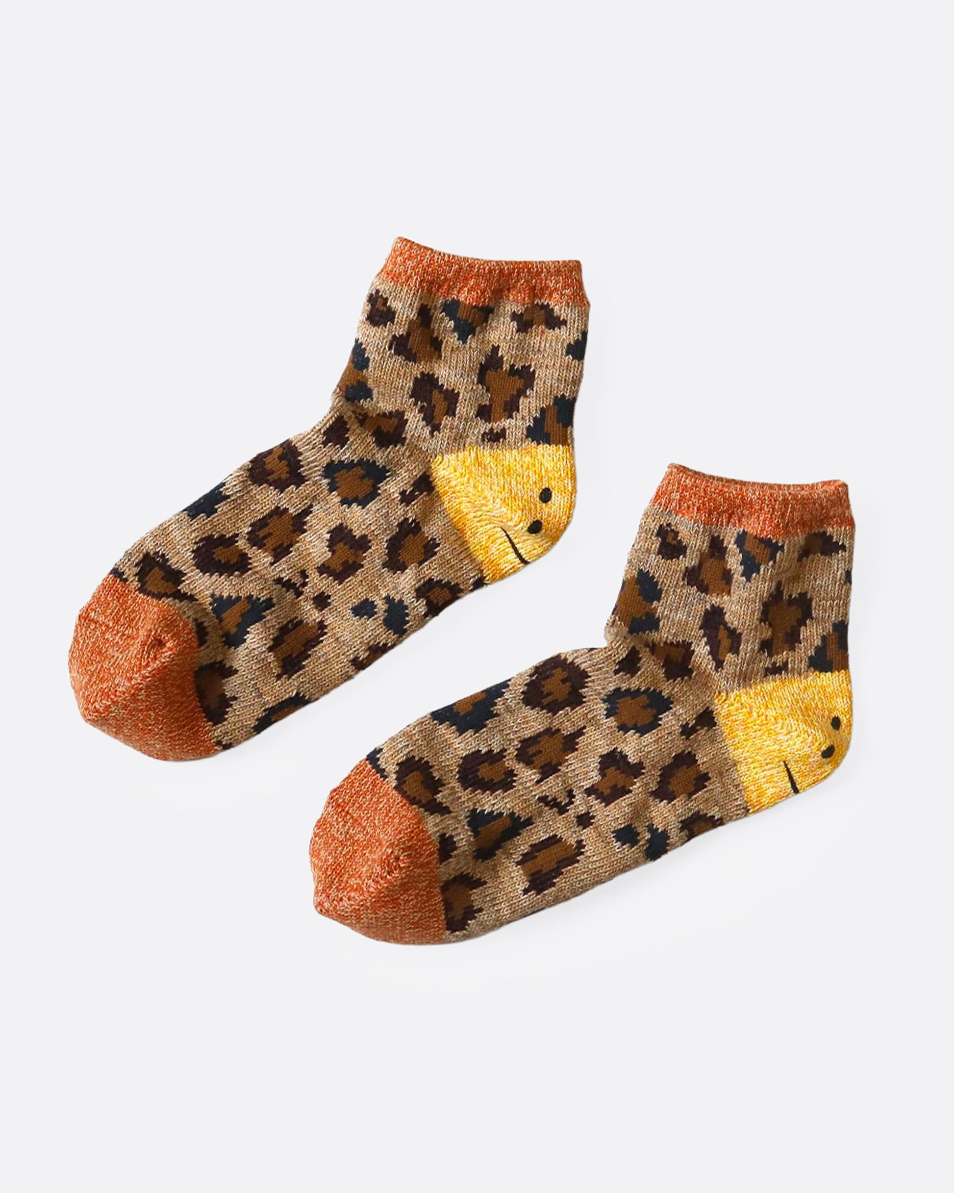 A pair of leopard print ankle socks with smiley faces of each heel. Shown from the side.