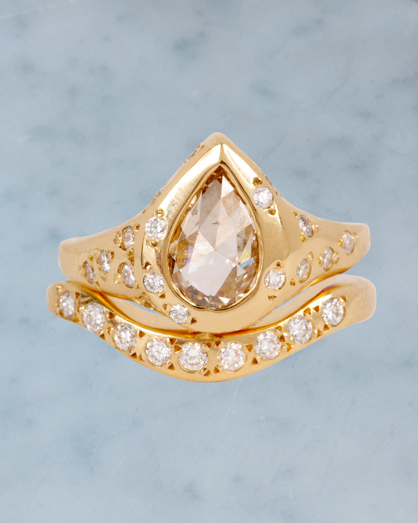 A rose cut, pear shaped, rustic diamond is set in a ring covered in round white diamond stars.