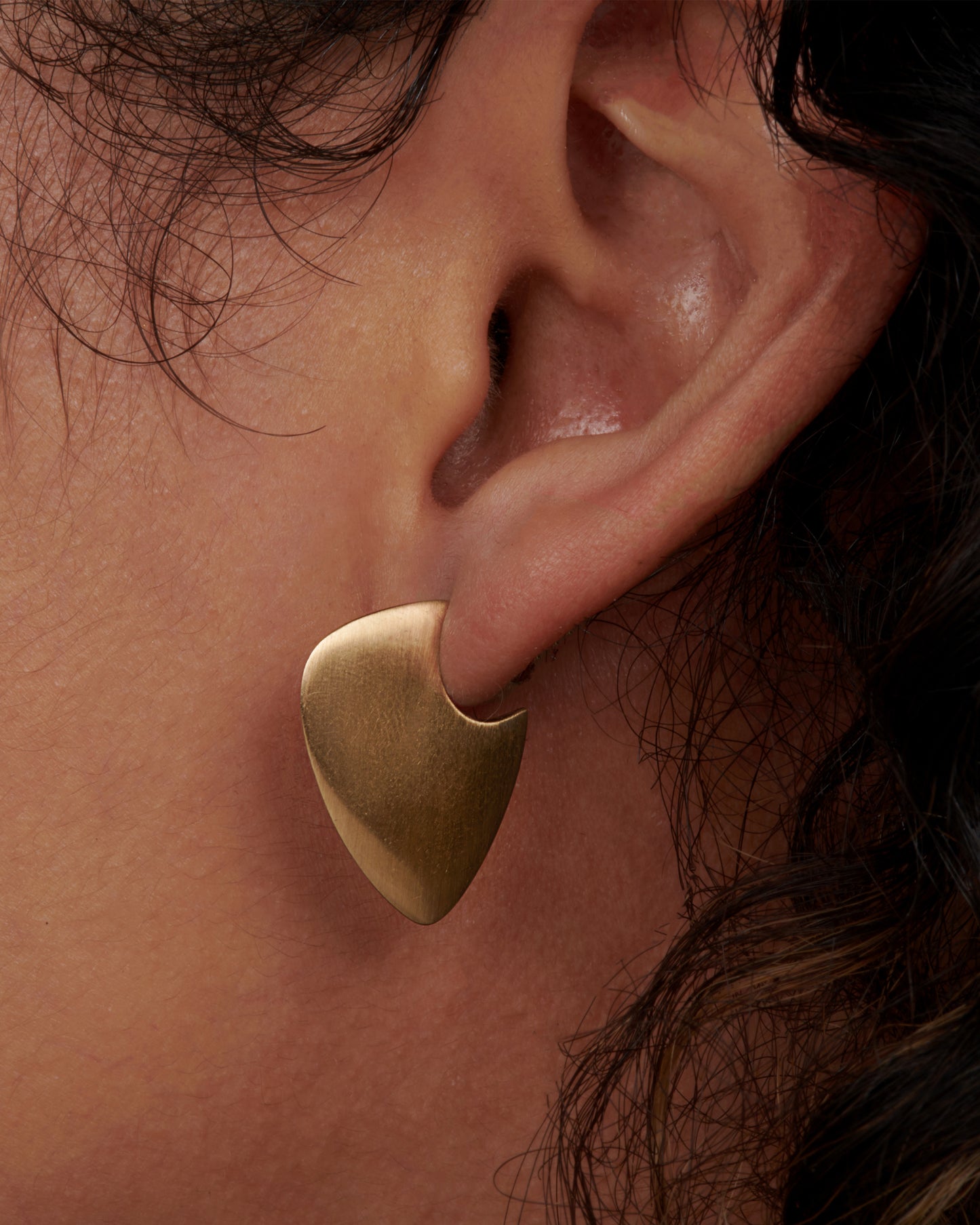 A pair of 10k solid gold hoop earrings with a guitar pick shape. View on an ear.