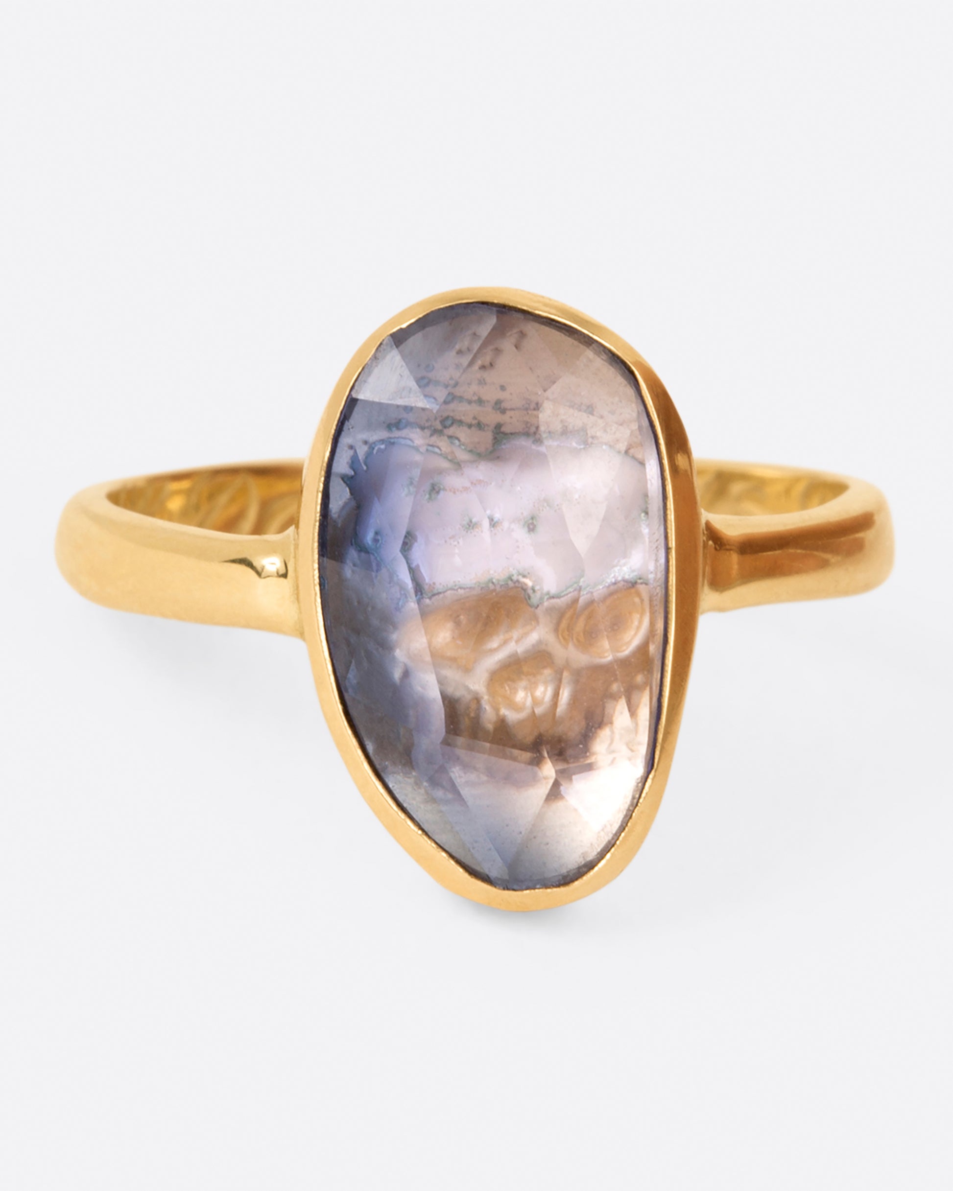 A ring featuring an oval rose cut blue sapphire with a carved skull behind it, shown from the front.