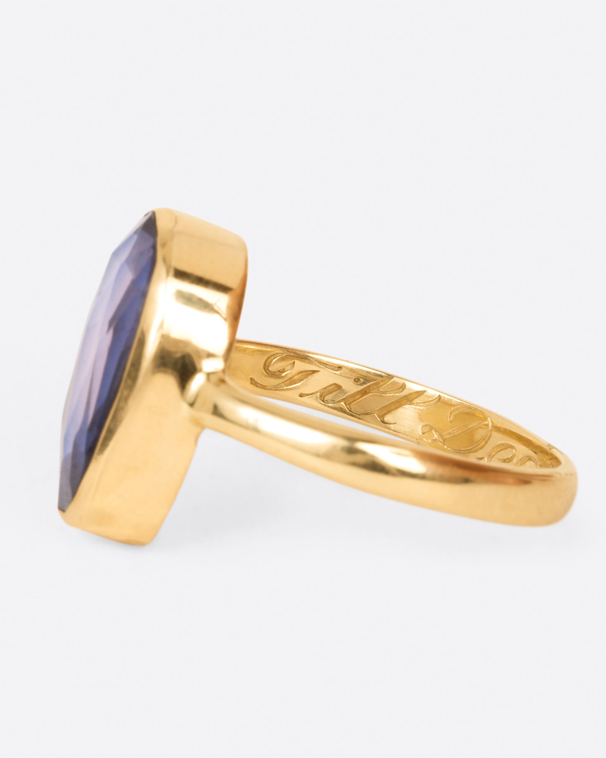 A ring featuring an oval rose cut blue sapphire with a carved skull behind it, shown from the side.