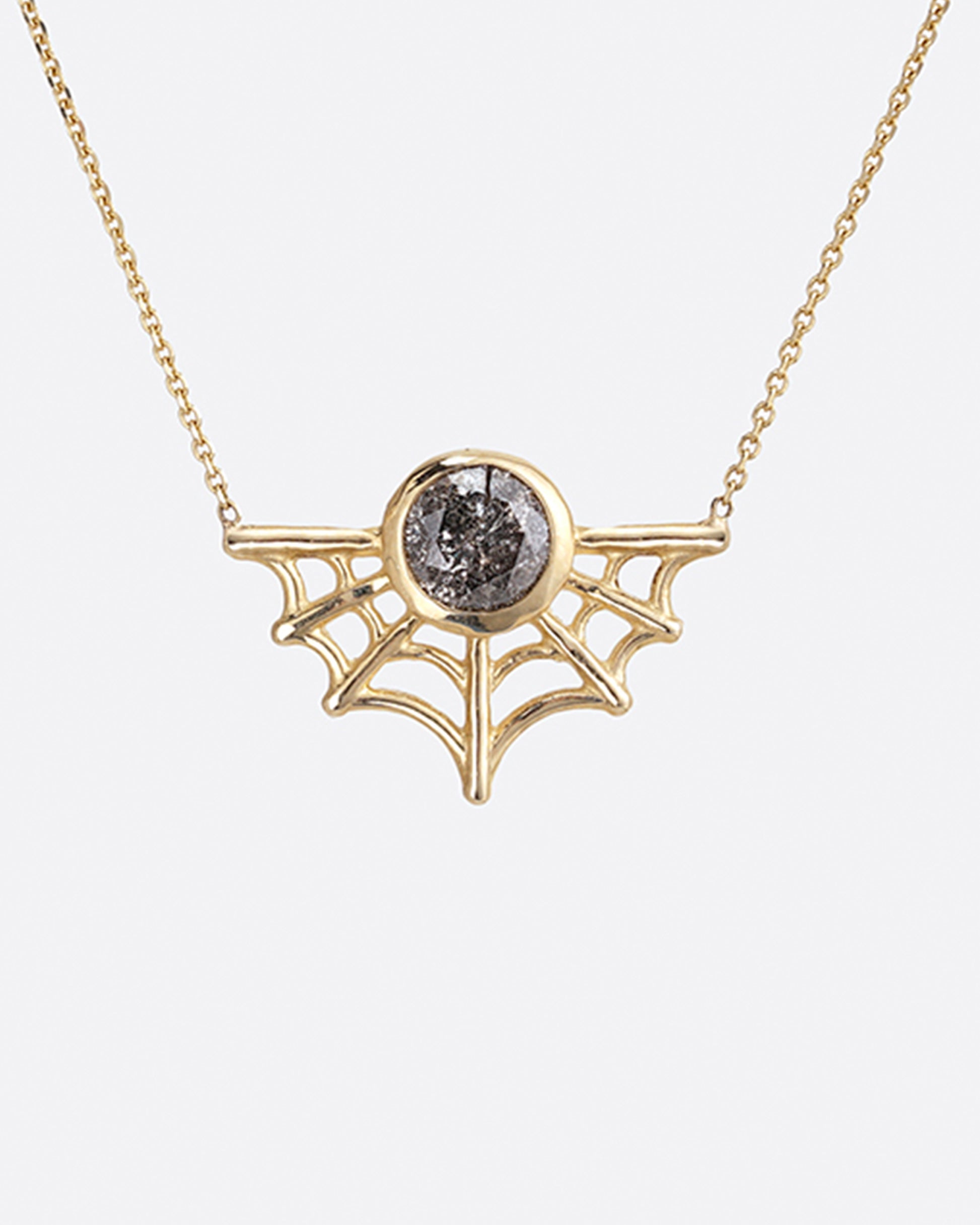 A curved spider web necklace with a bezel set salt and pepper diamond nestled in the middle.