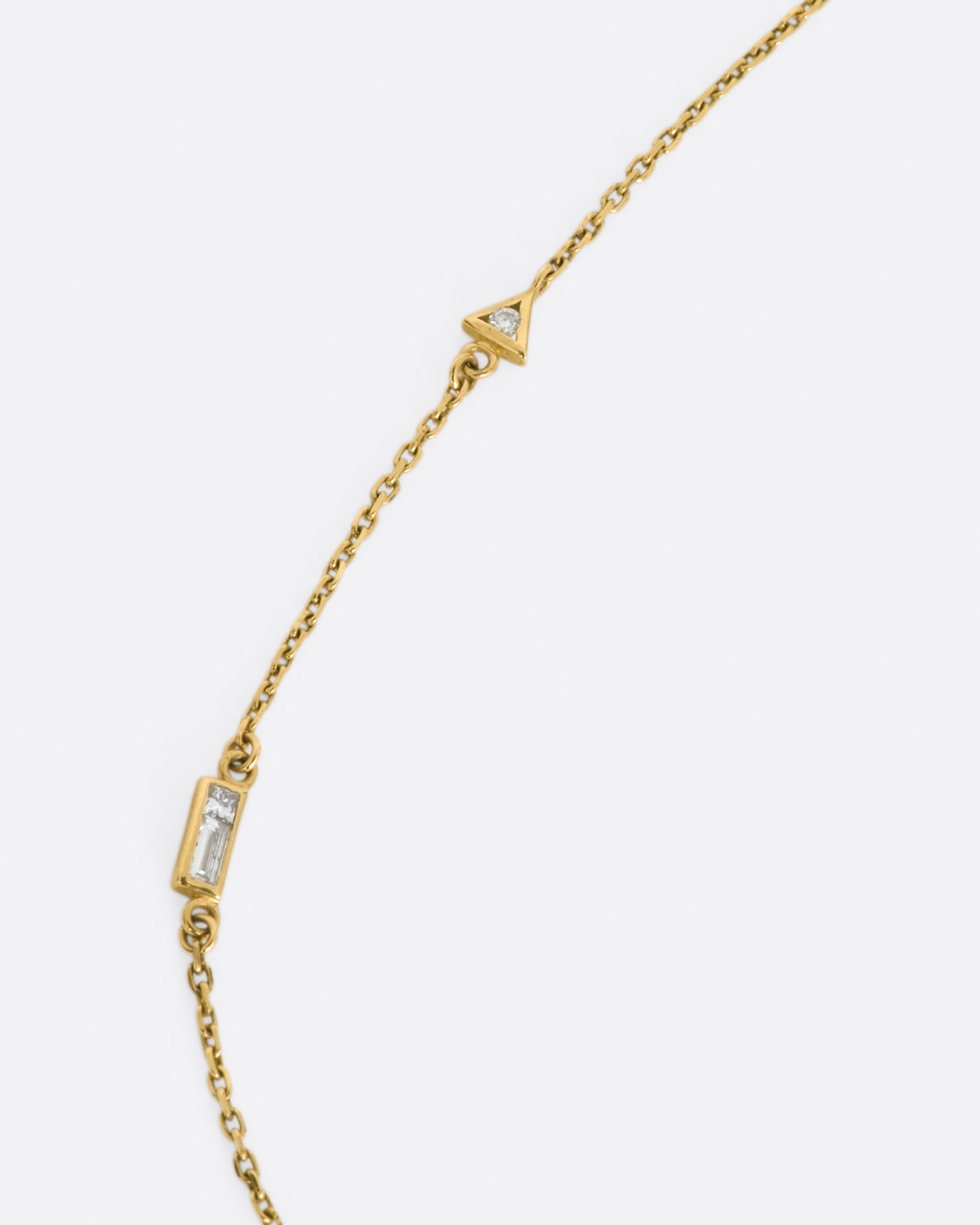 A yellow gold cable chain necklace with a round diamond in a triangular setting and a baguette diamond in a rectangular setting, set into the chain about an inch apart.