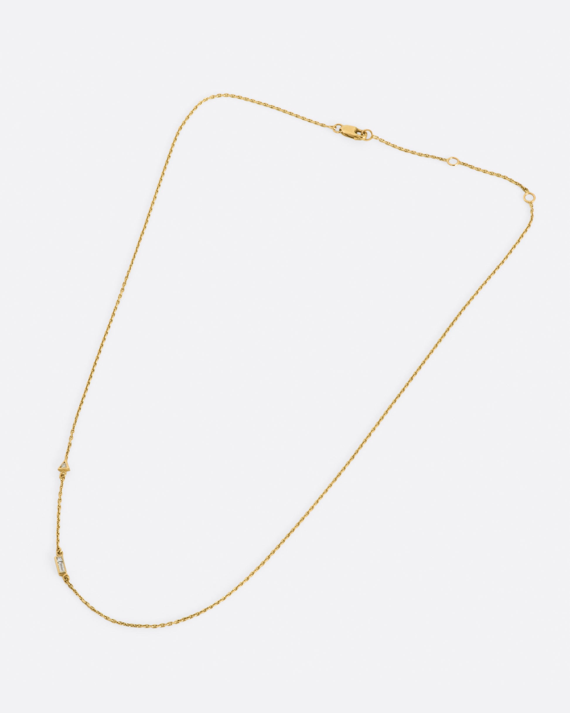 A yellow gold cable chain necklace with a round diamond in a triangular setting and a baguette diamond in a rectangular setting, set into the chain about an inch apart.