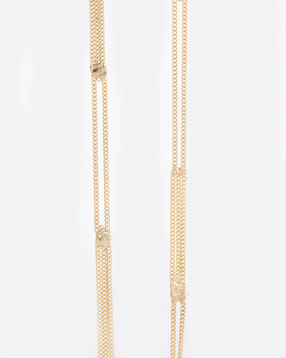 A long yellow gold multi chain necklace with alternating pattern of squares finished with gold solder, shown close up.