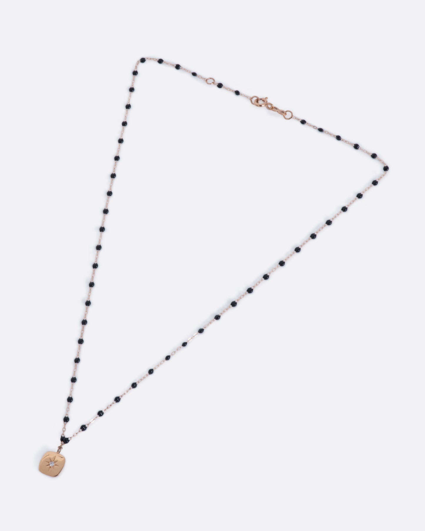 A classic rose gold Gigi Clozeau necklace with black resin beads and a square tag pendant, with a star-set diamond at its center