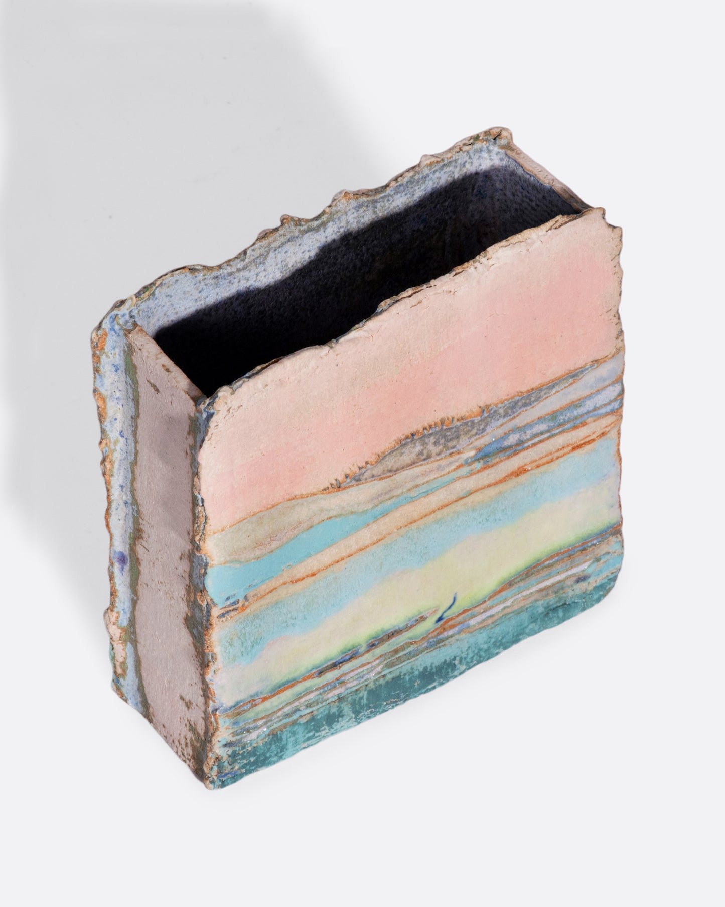 A ceramic vessel meticulously handmade with many layers of glaze atop stoneware clay. The rich, varied texture becomes a beautiful canvas for an ethereal landscape like you're gazing over a lake while the sunsets golden over hills in the distance.