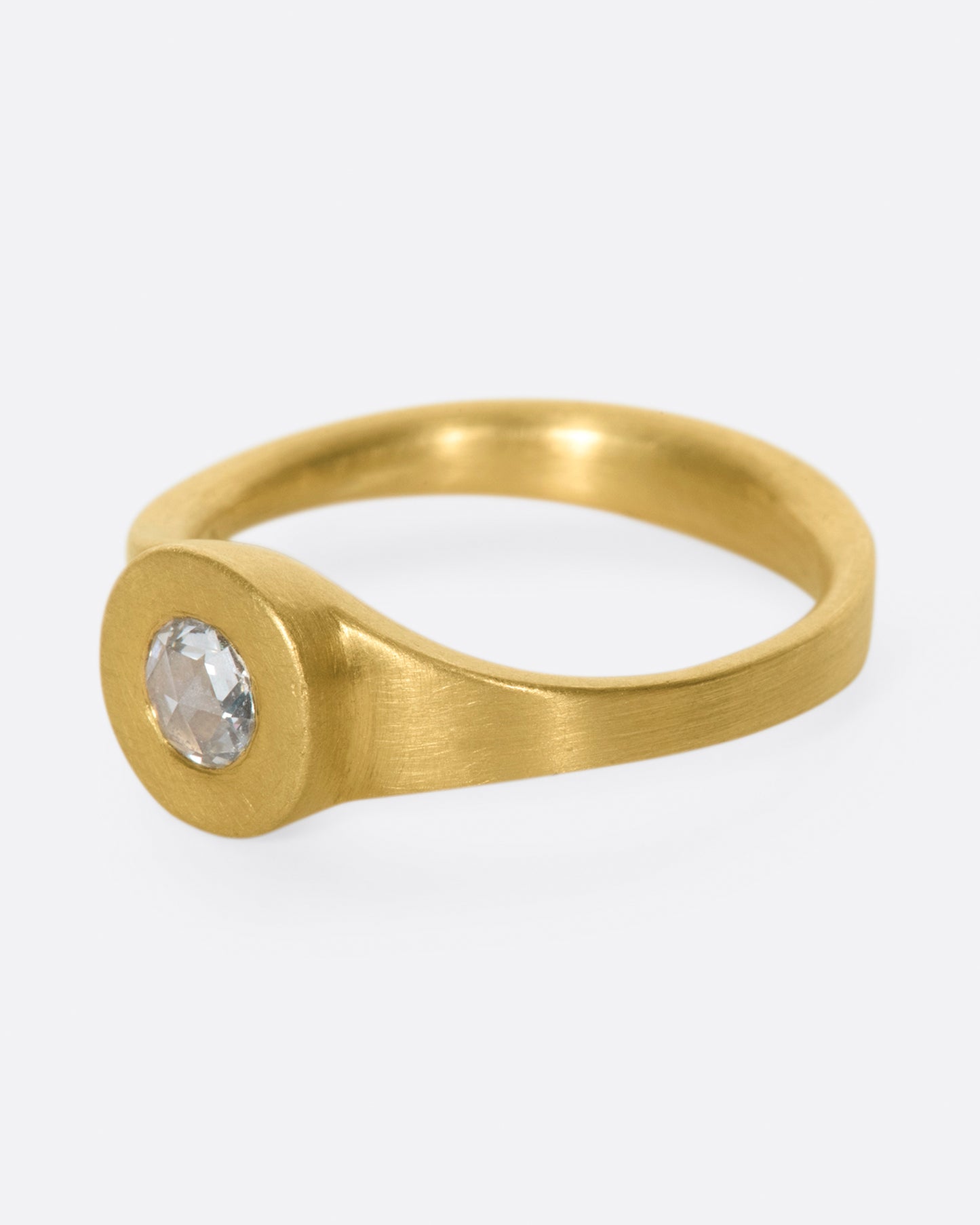 A rose cut diamond sits at the center of this hand carved, matte gold ring.