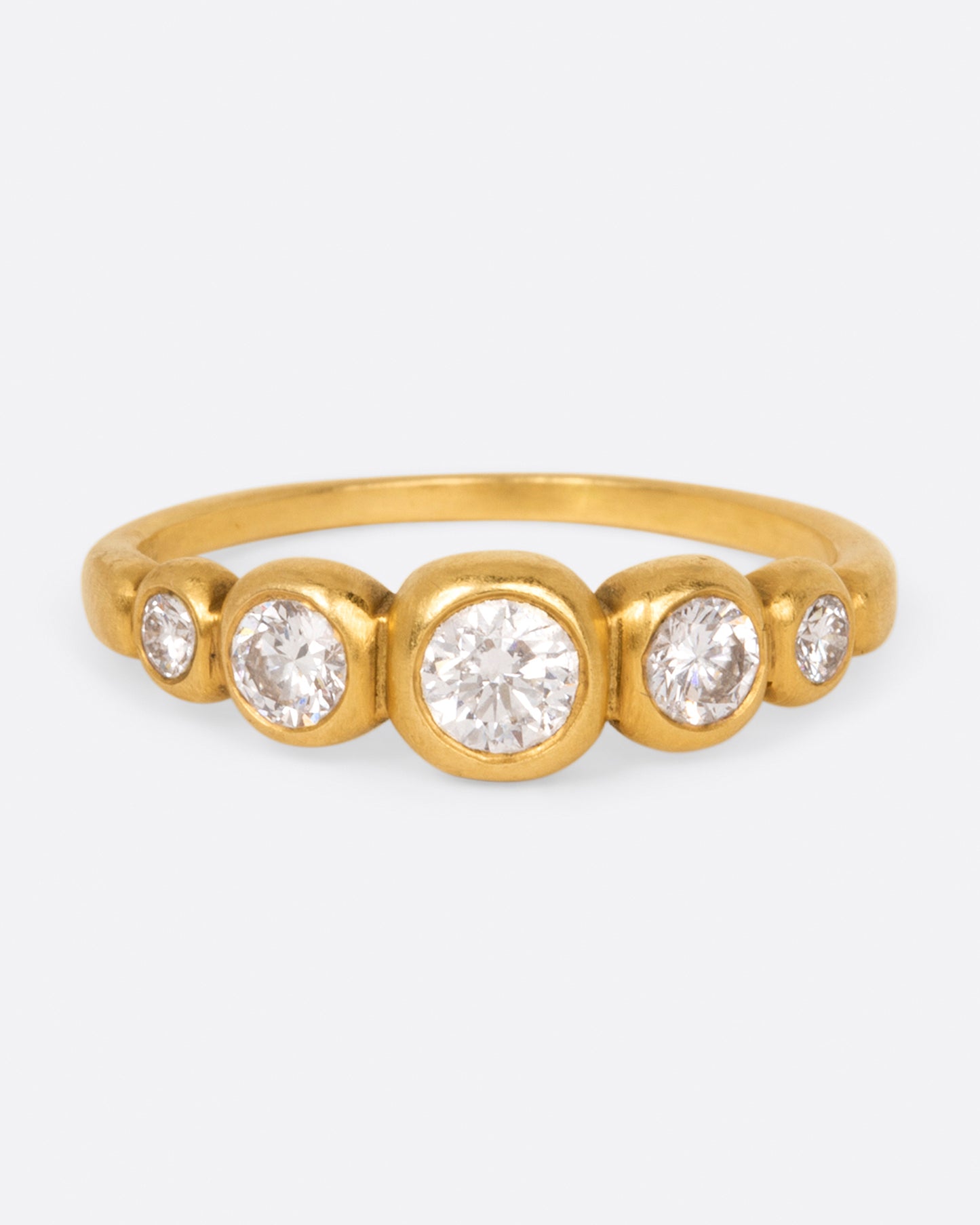A brushed gold ring with five round white diamonds in graduated sizes, shown from the front.