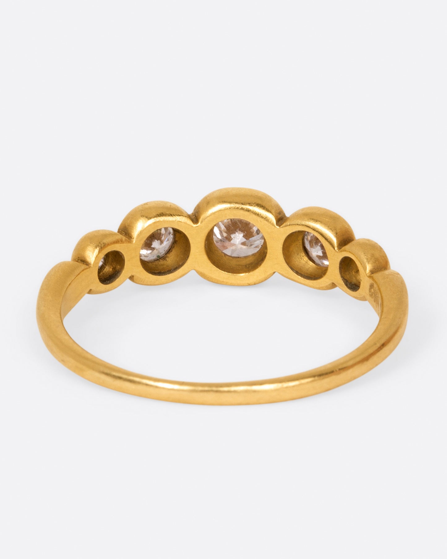 A brushed gold ring with five round white diamonds in graduated sizes, shown from the back.