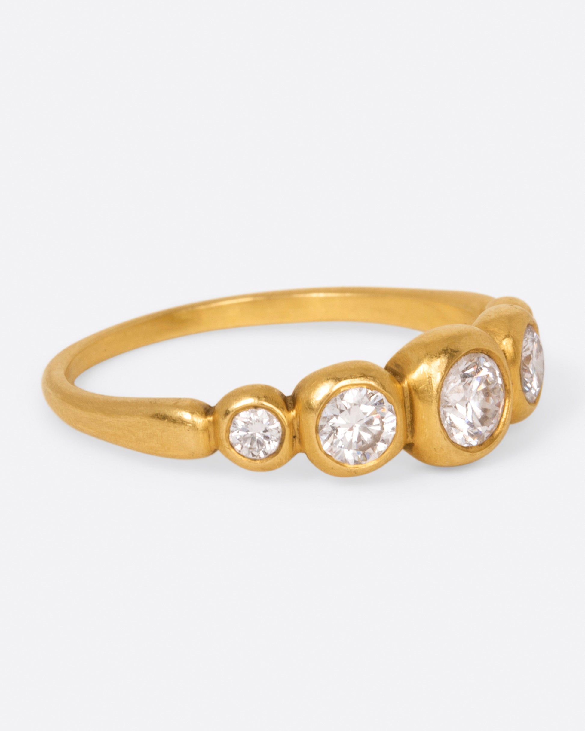 A brushed gold ring with five round white diamonds in graduated sizes, shown from the side.