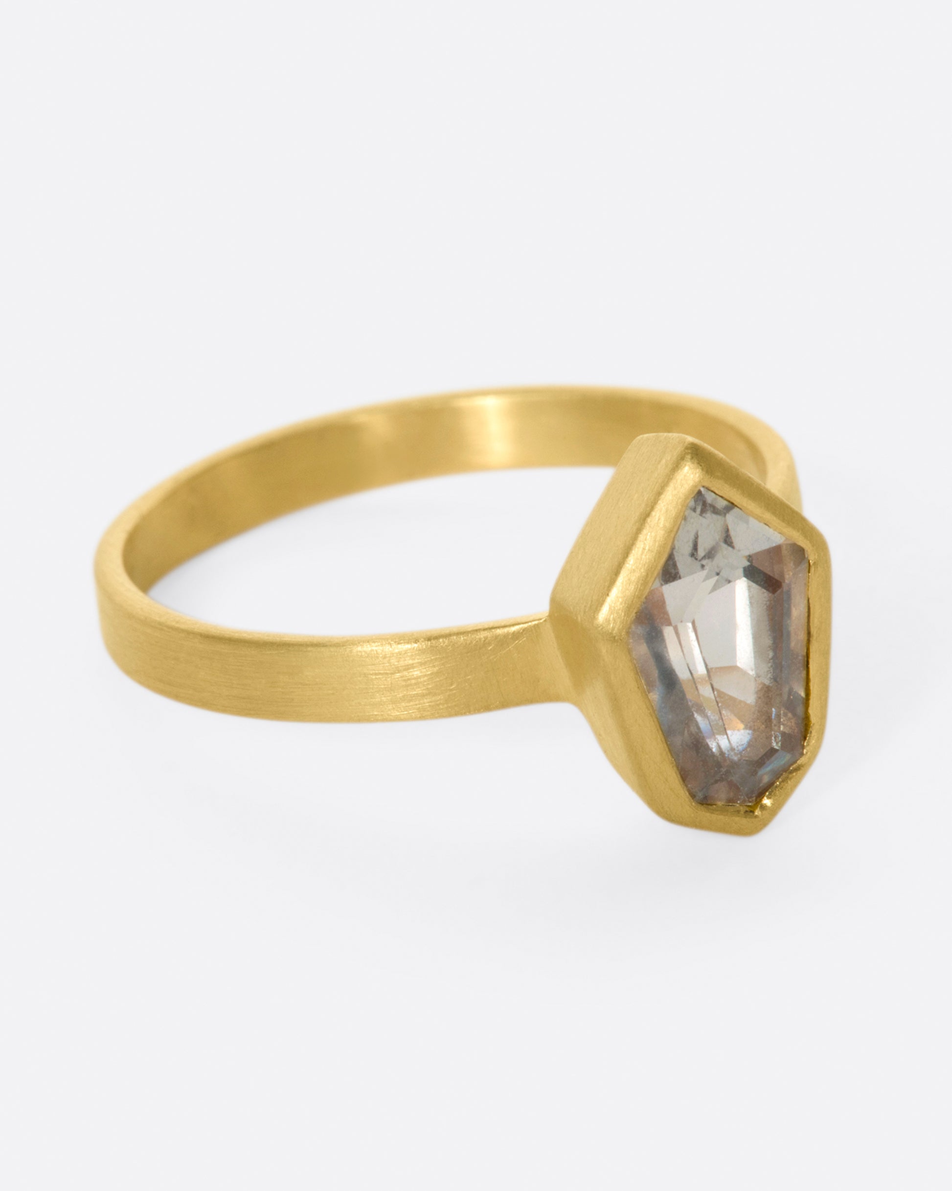 A matte gold solitaire ring with a bezel set, shield shaped sapphire.