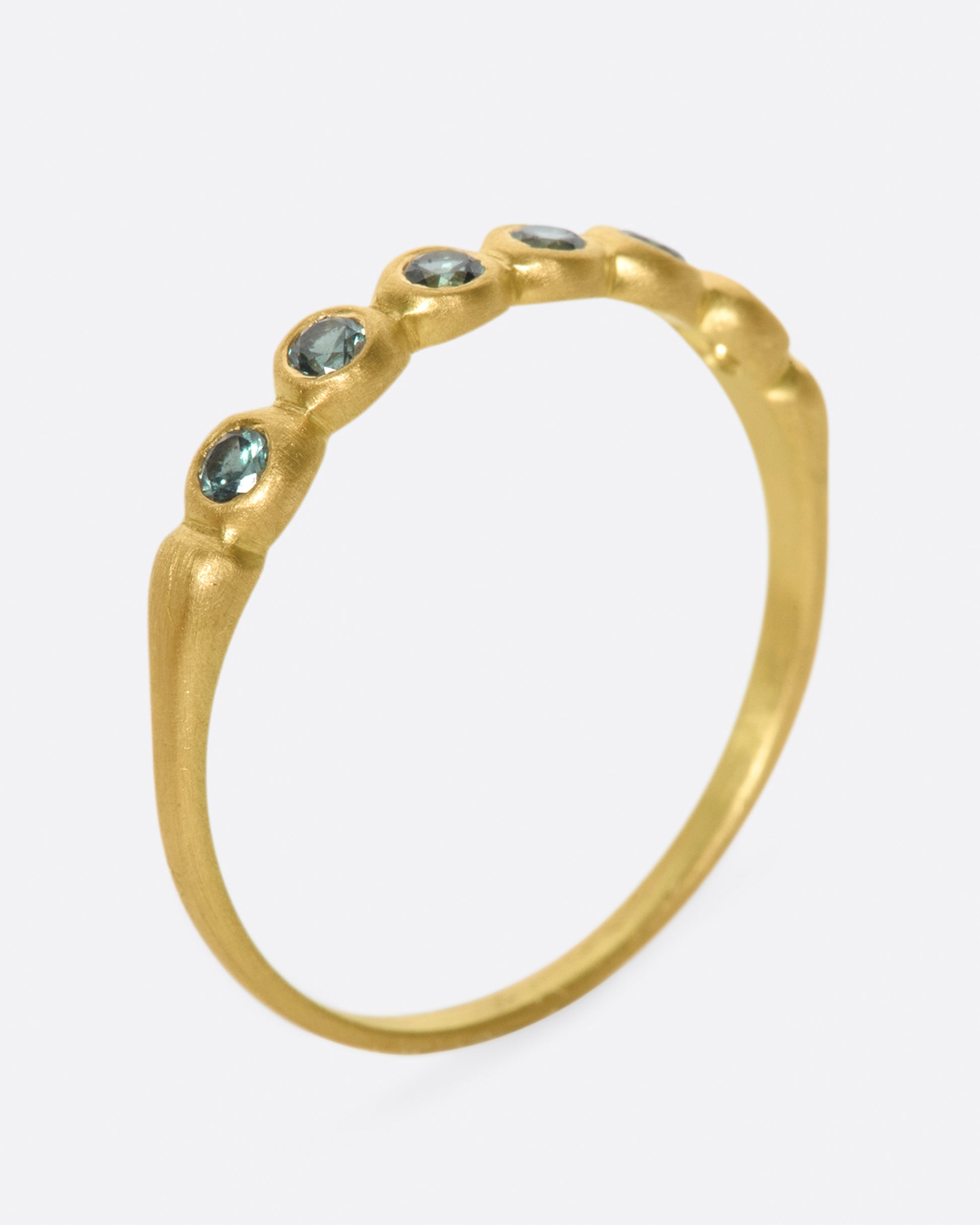 A matte gold band with teal green sapphires almost halfway around.