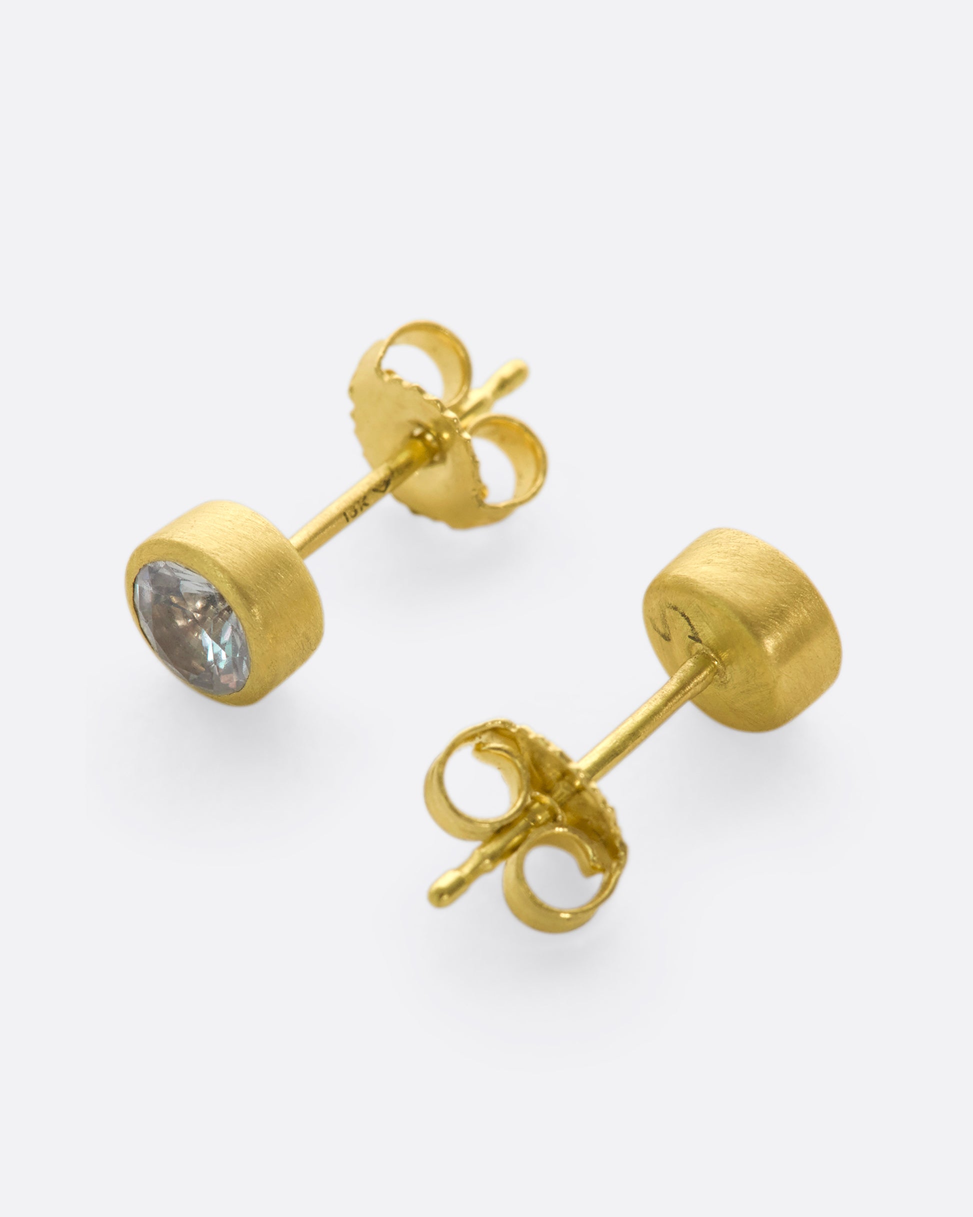 A pair of yellow gold solitaire earrings with round white sapphires in bezel settings.