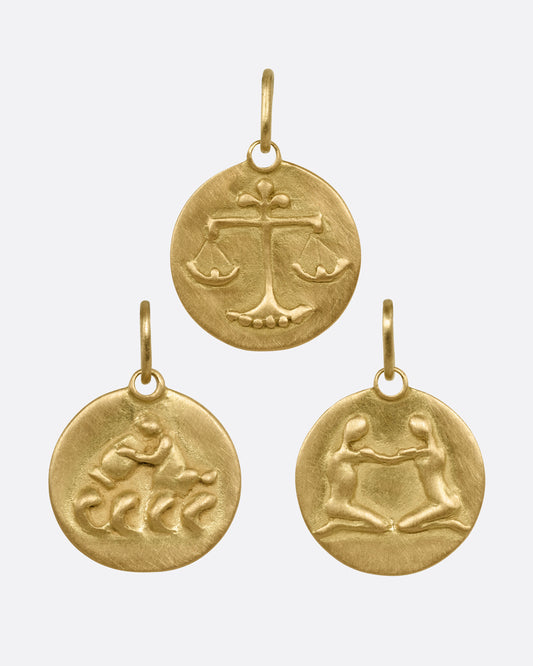 Three circular yellow gold zodiac pendants- one Libra, one Aquarius, and one Gemini, shown from the front.