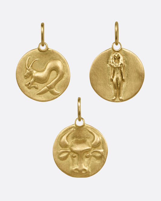 Three circular yellow gold zodiac pendants- one Capricorn, one Virgo, and one Taurus, shown from the front.