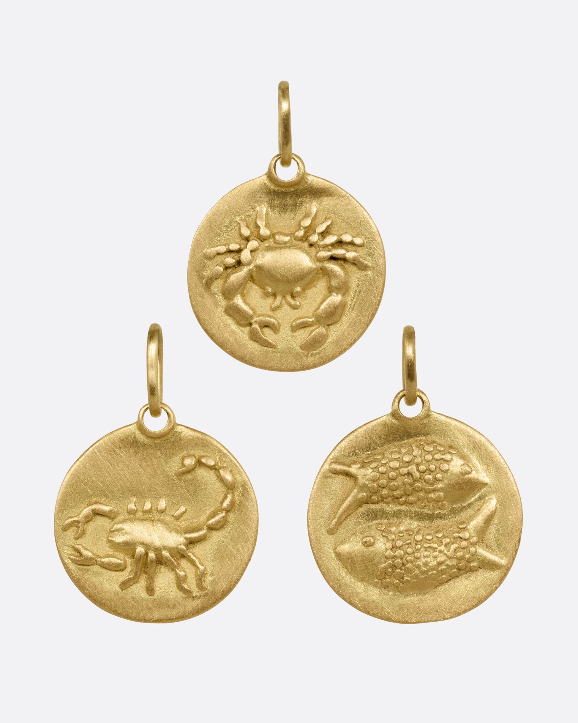 Three circular yellow gold zodiac pendants- one Cancer, one Scorpio, and one Pisces. Shown from the front.