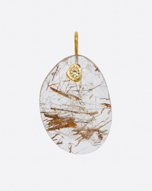 A yellow gold charm featuring a slice of rutilated quartz, with a yellow sapphire at its center.