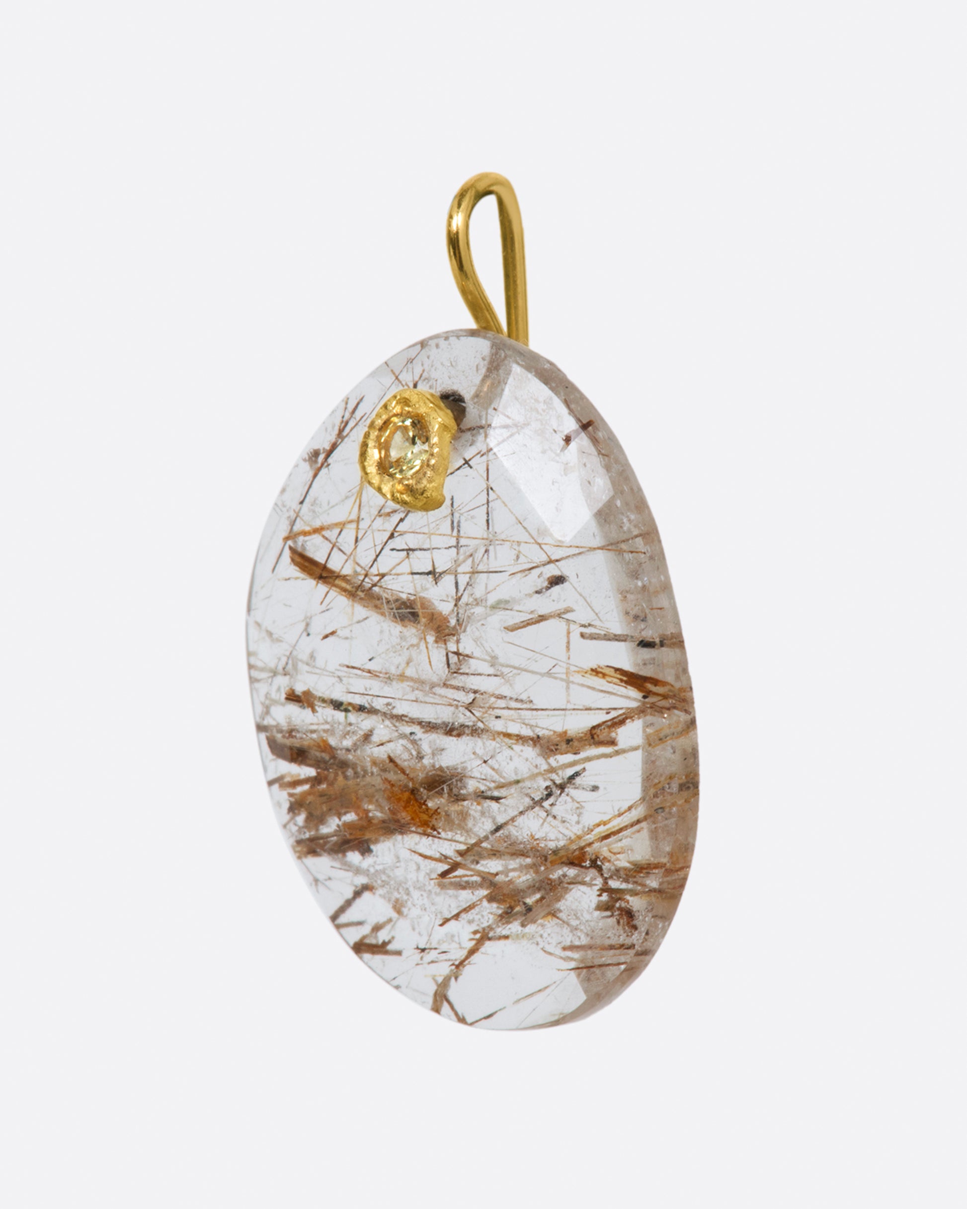 A yellow gold charm featuring a slice of rutilated quartz, with a yellow sapphire at its center. Shown from the side.