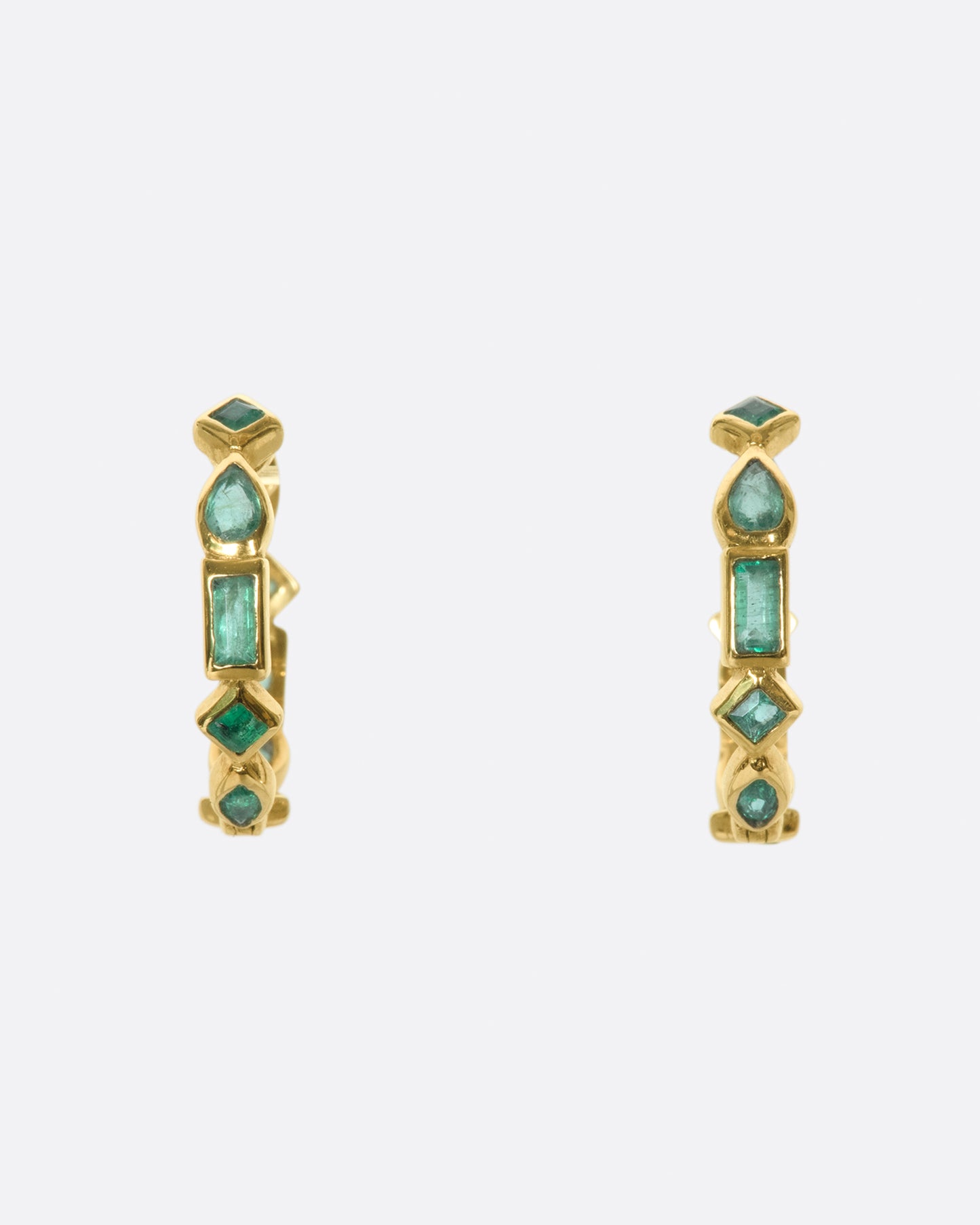 A pair of of huggie hoops made from a mosaic of baguette, pear, round, and princess cut emeralds.