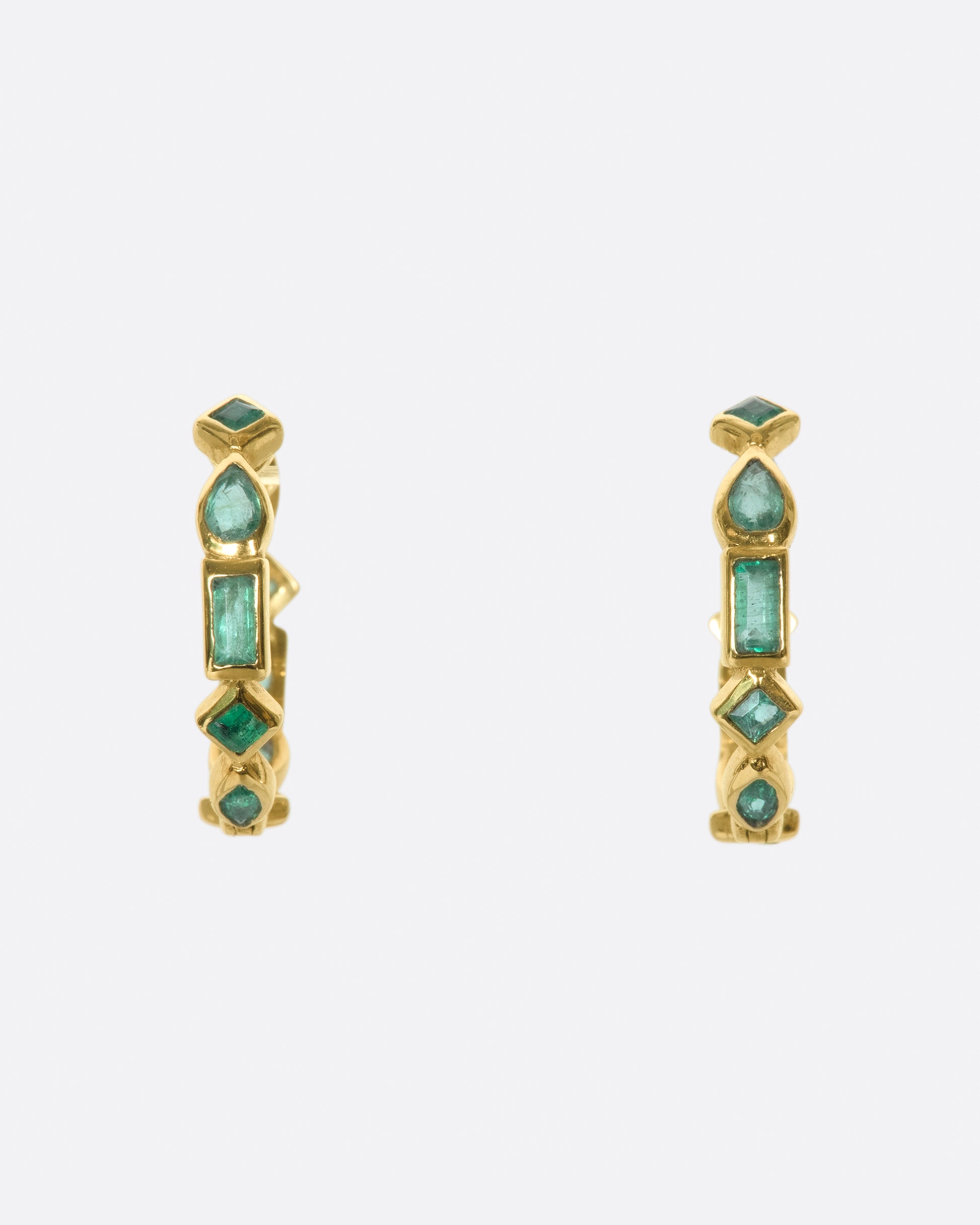 A pair of of huggie hoops made from a mosaic of baguette, pear, round, and princess cut emeralds.