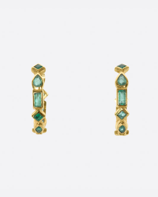 A pair of of huggie hoops made from a mosaic of baguette, pear, round, and princess cut emeralds.