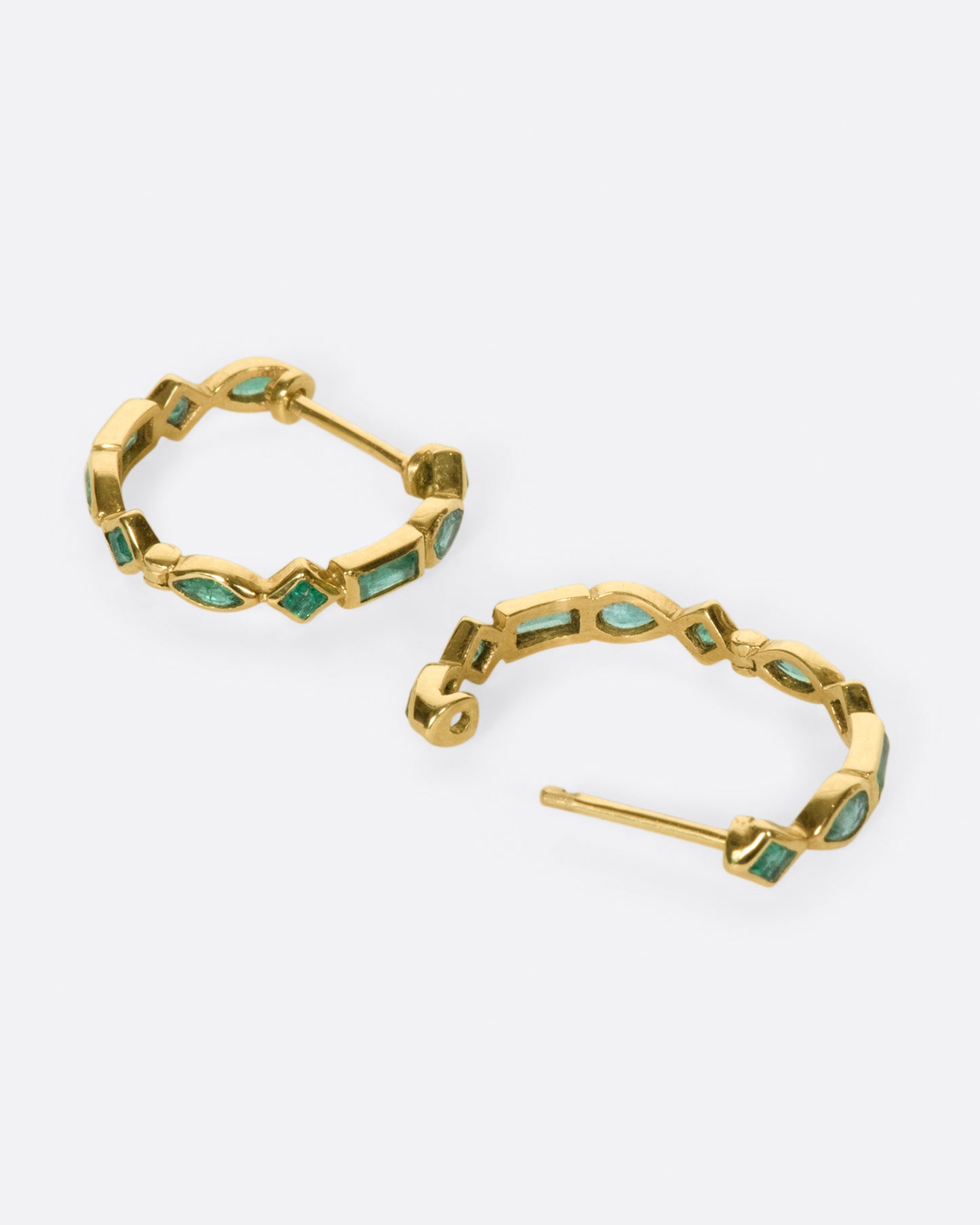 A pair of of huggie hoops made from a mosaic of baguette, pear, round, and princess cut emeralds.