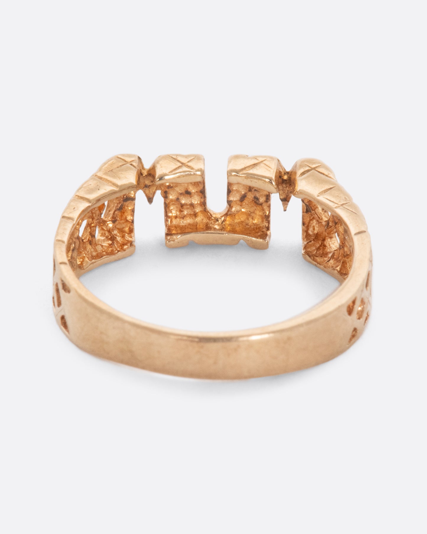 Gold ring that reads 'MUM' with crosshatch retail on either side. View from the back.