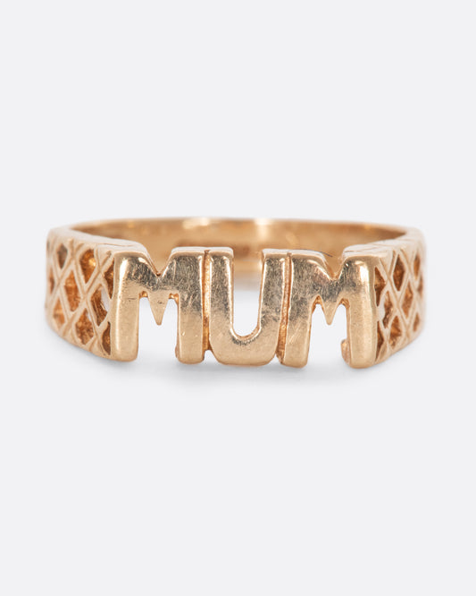 Gold ring that reads 'MUM' with crosshatch retail on either side. View from the front.