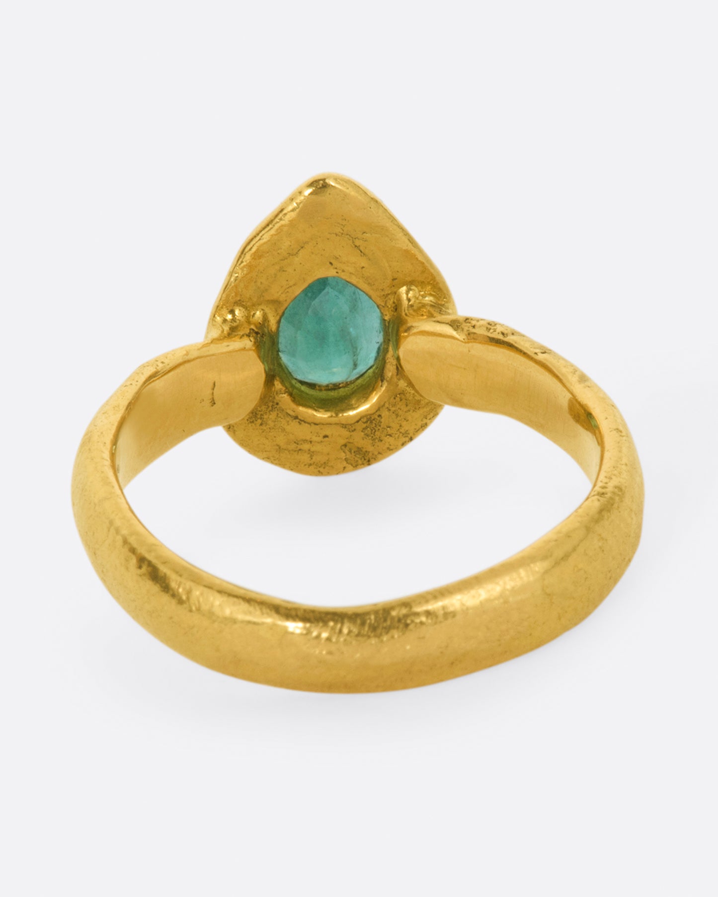 A high karat gold ring with an organic shaped band and a pear shaped emerald at its center with a sunken round emerald halo. Shown from the back.