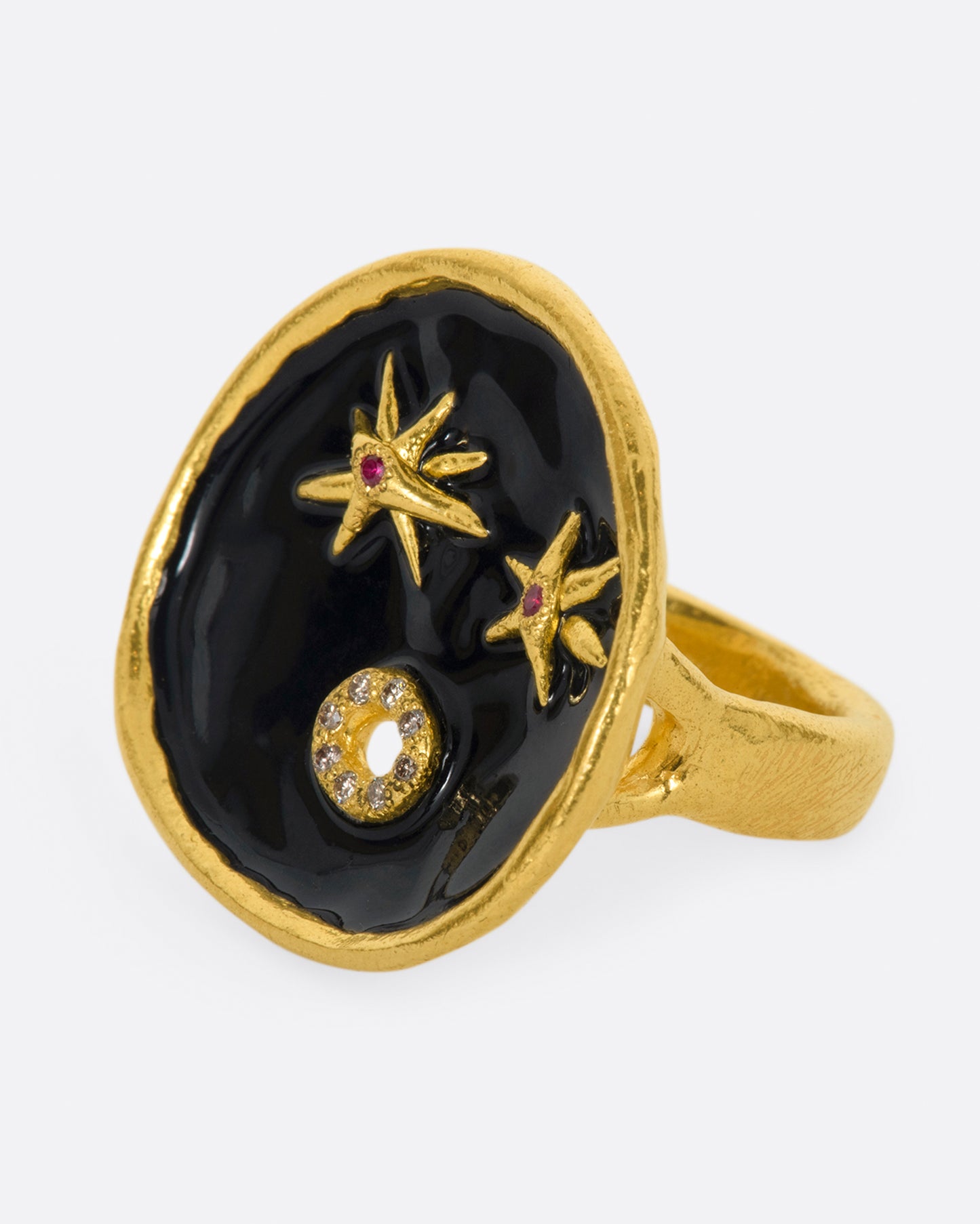 A large high karat gold ring with a round black enamel face, ruby star eyes and a open mouth covered in diamonds. Shown from the side.