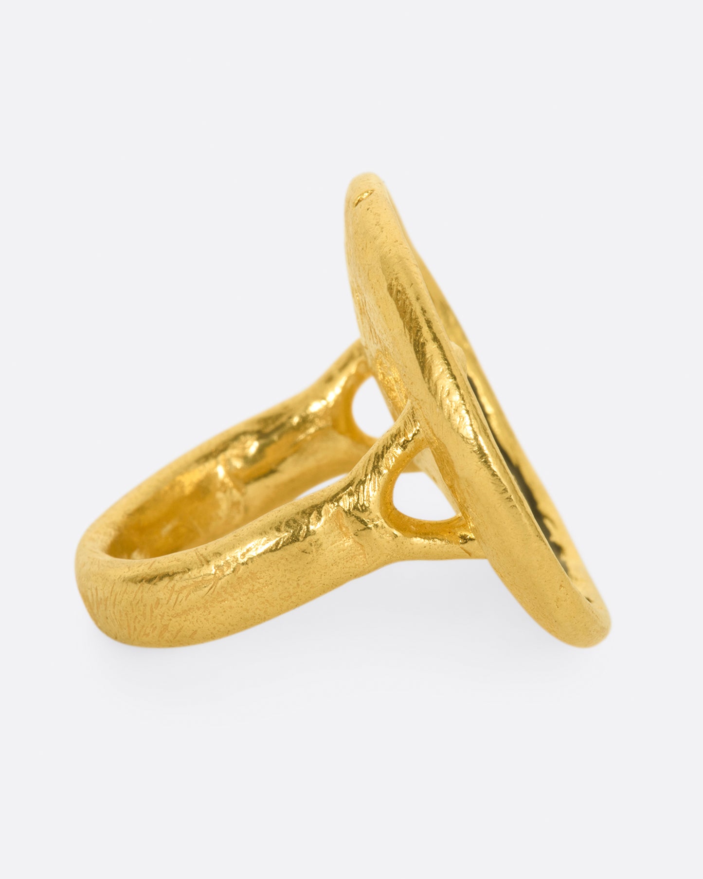 A large high karat gold ring with a round black enamel face, ruby star eyes and a open mouth covered in diamonds. Shown from the side.