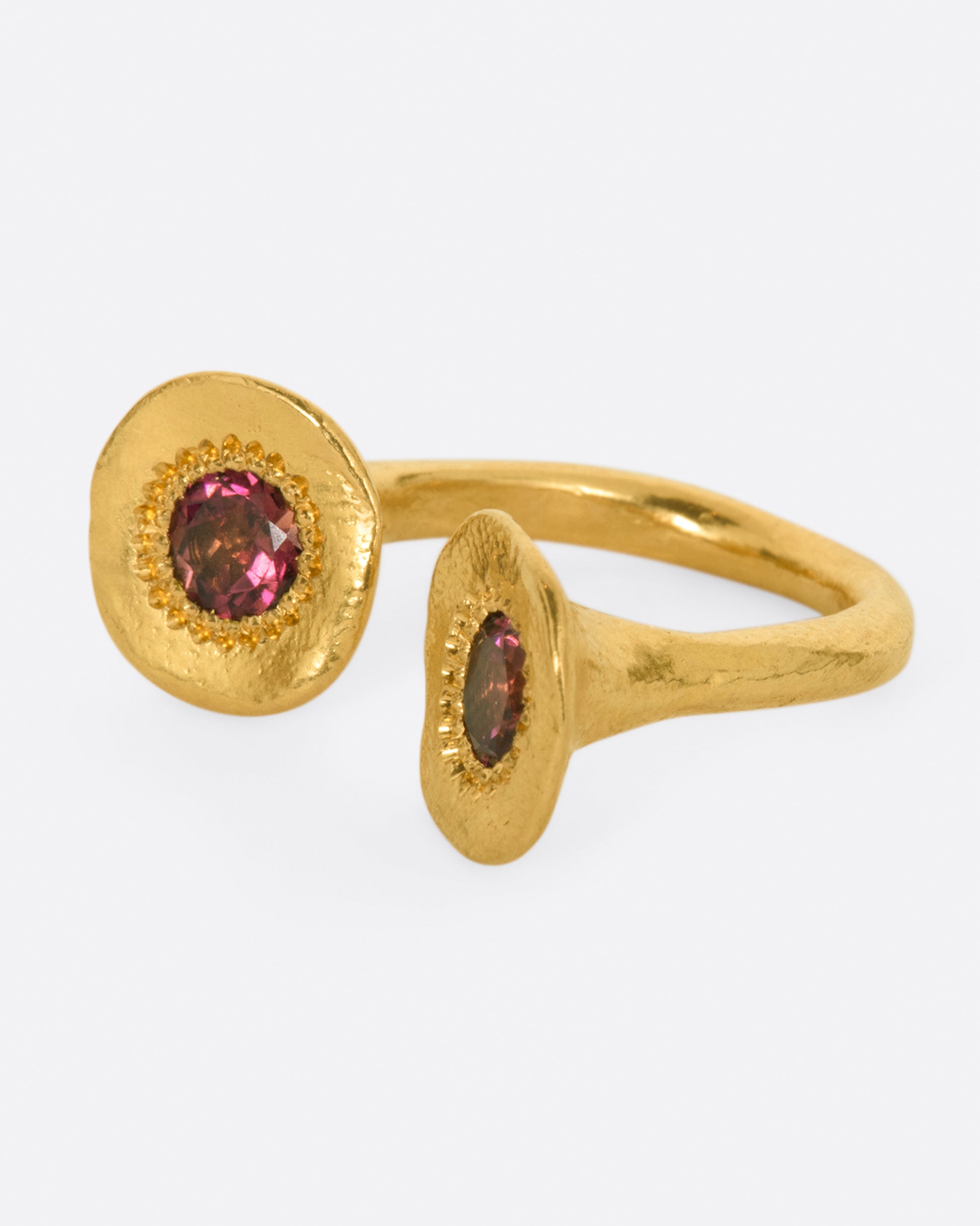 A high karat gold open ring with a large organic shaped disc on each end with a rosey pink tourmaline at its center. Shown from the side.