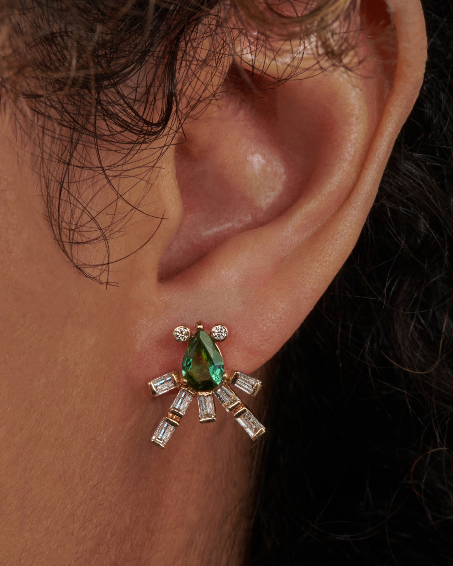 This gorgeous green tourmaline earring is swimming with sage and rich forrest green tones. Round diamond accents and glimmering baguettes light up beneath your lobe, creating an elegant, regal look. View on an ear.