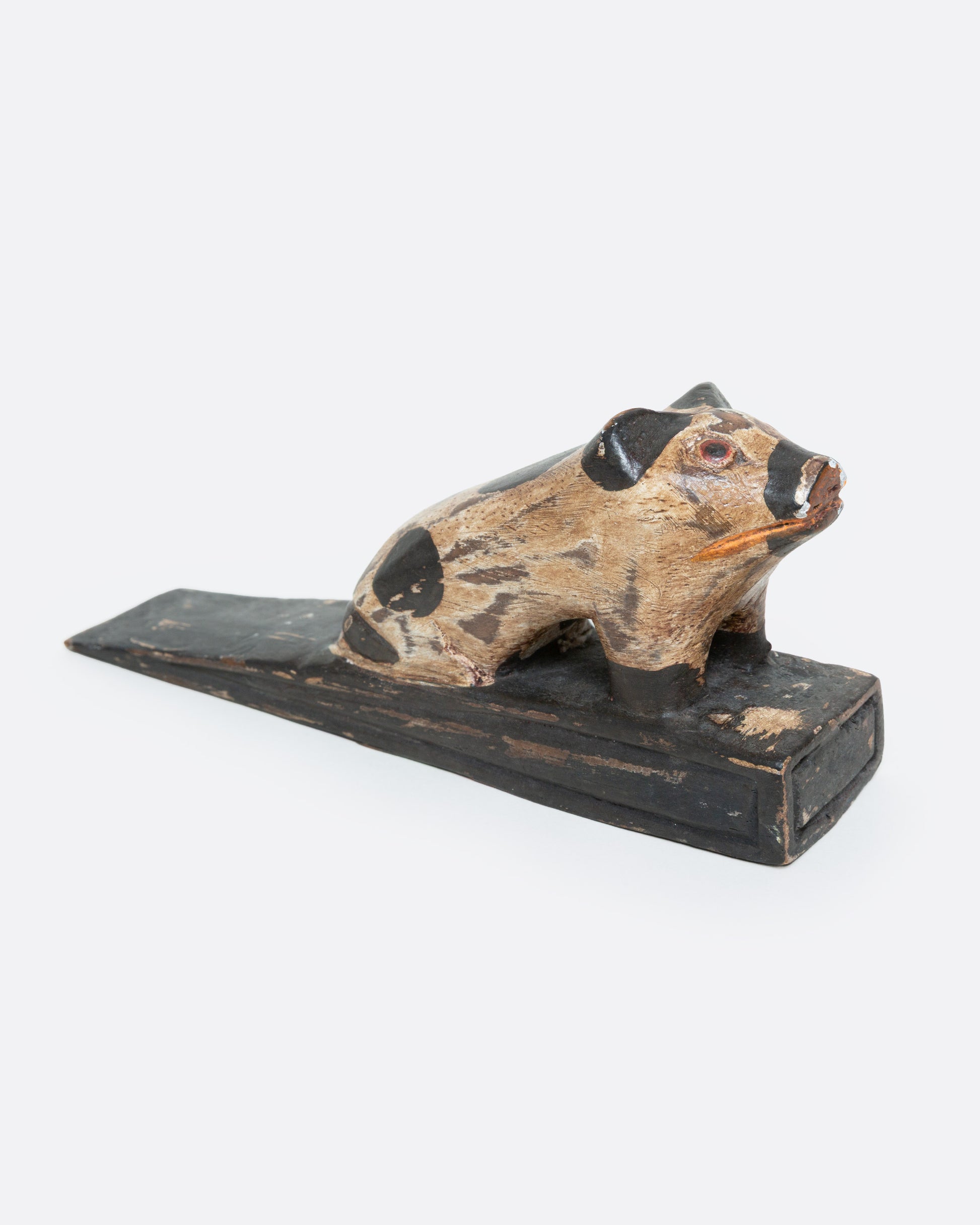 A hand carved wooden door stop with a spotted pig, shown from the side.